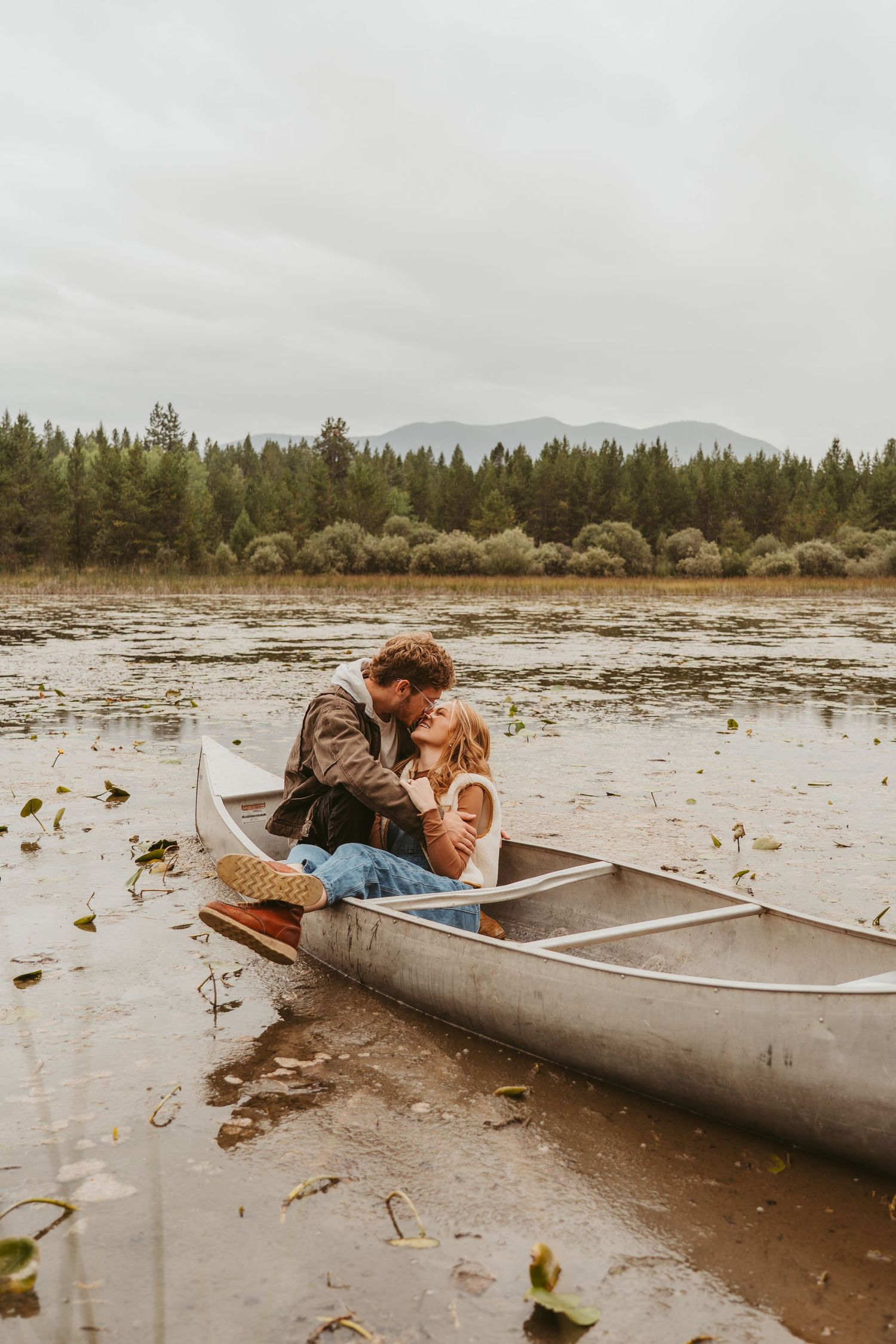 Couple relaxing together in a canoe on a shallow lake surrounded by lily pads and pine forest.