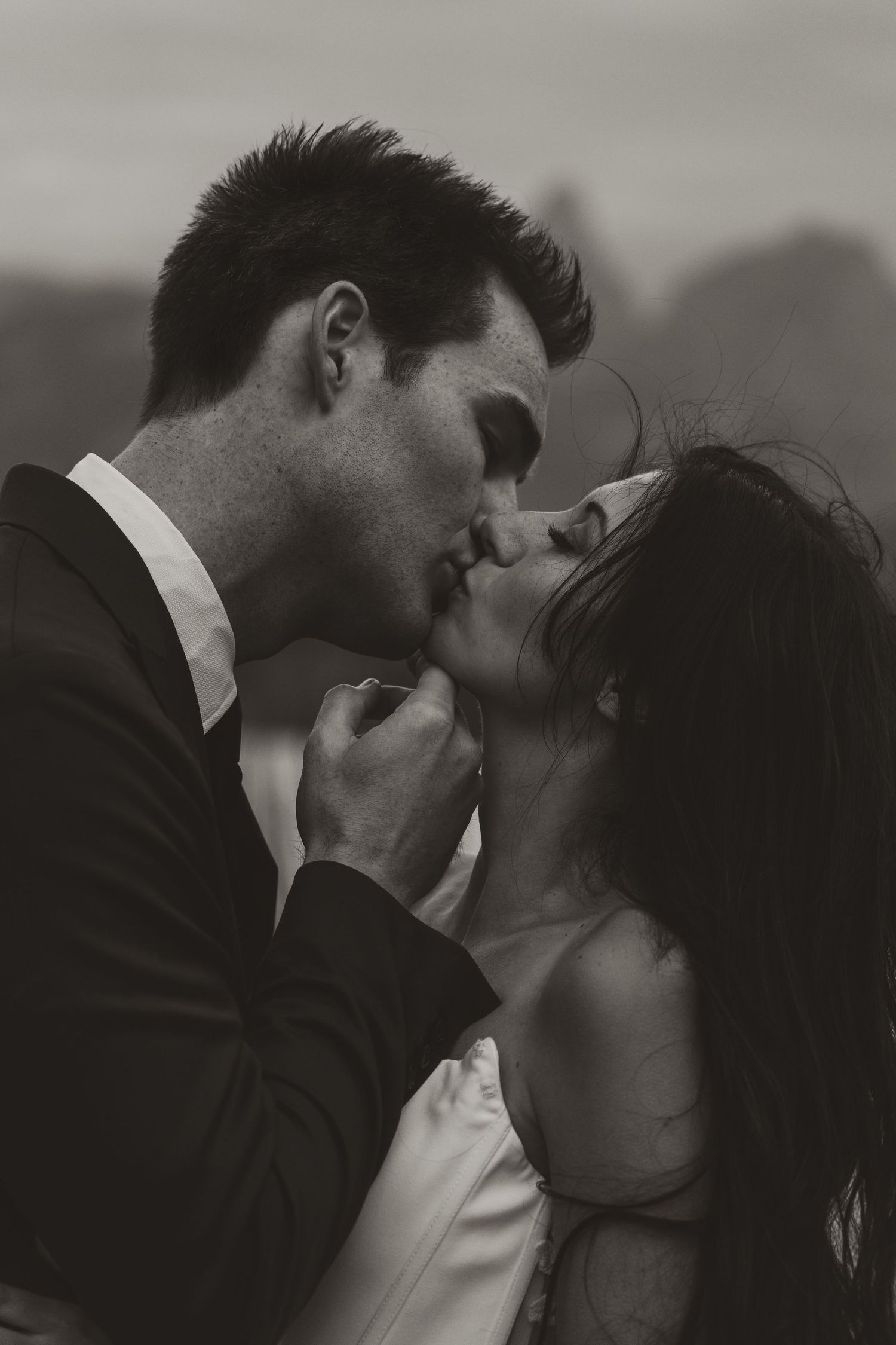 Black and white photo of a couple sharing a romantic kiss, the man in a suit and woman in a white dress.