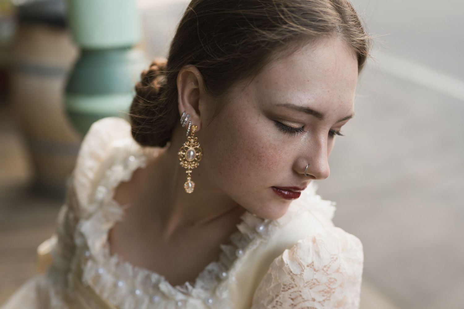 Bride with freckles wearing gold drop earrings and lace dress, hair in elegant updo, looking down gracefully.