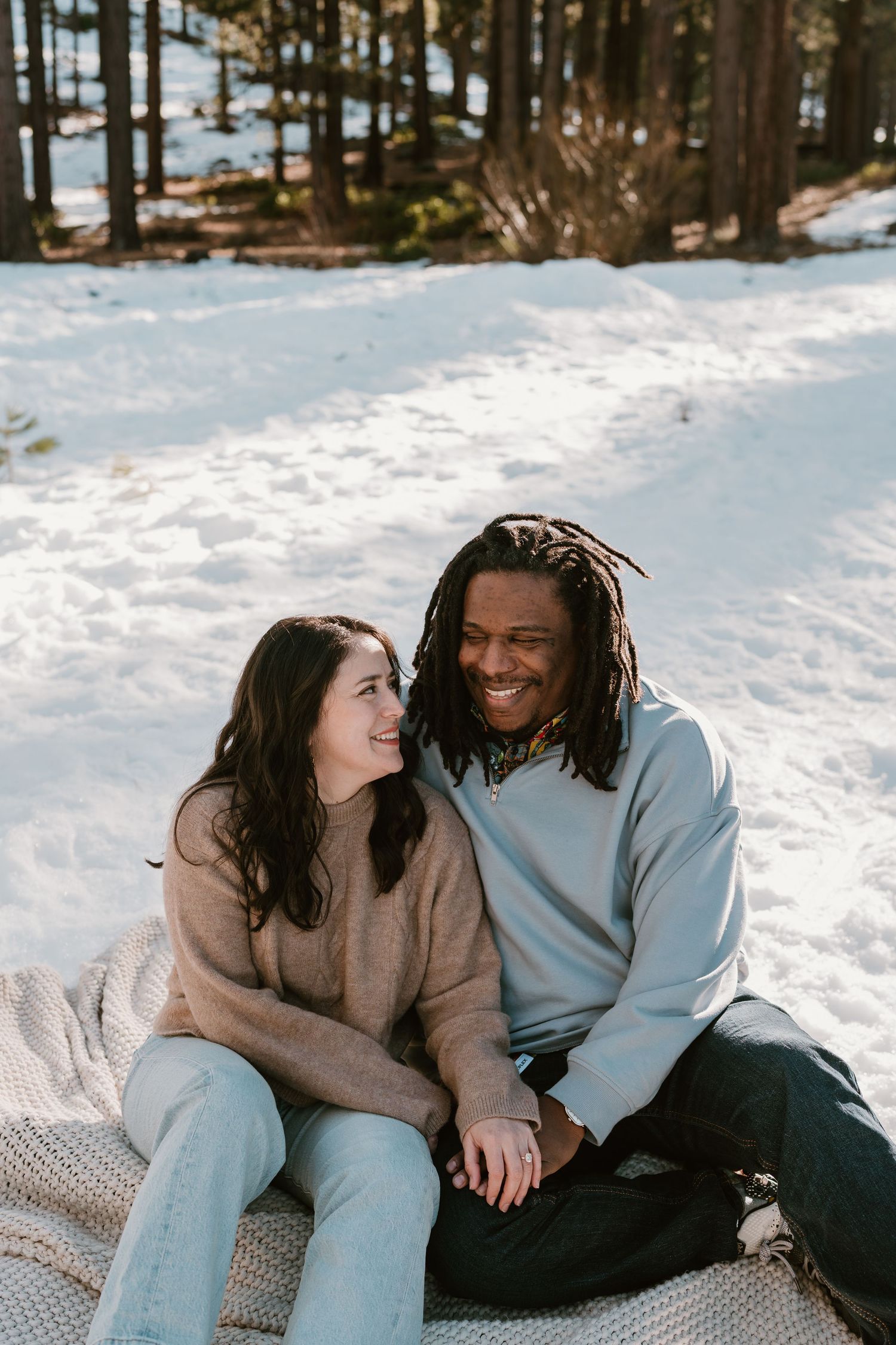 A couple sits together on snowy ground sharing intimate moments in a winter forest setting.