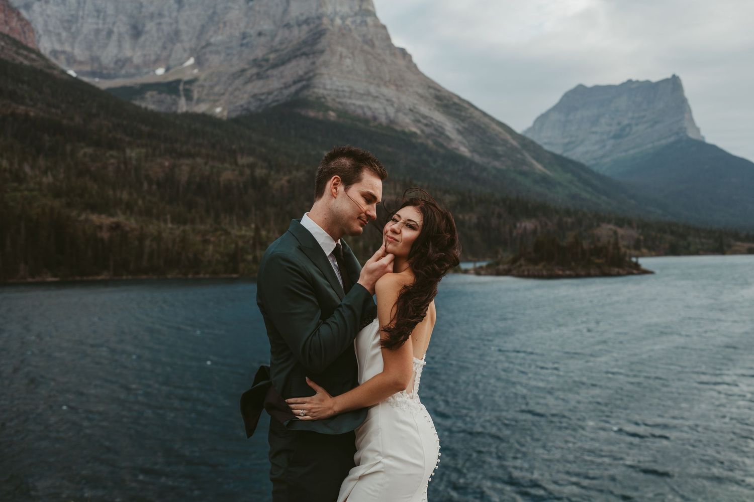 Two people share an intimate moment against a stunning mountain lake backdrop at Glacier National Park.