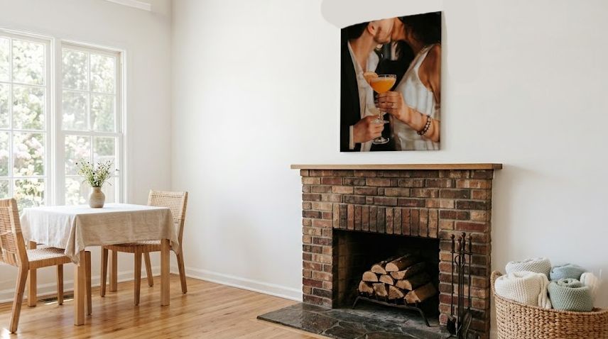 Bright living room with brick fireplace, wood mantel, and romantic couple canvas print above, featuring a dining area by window.