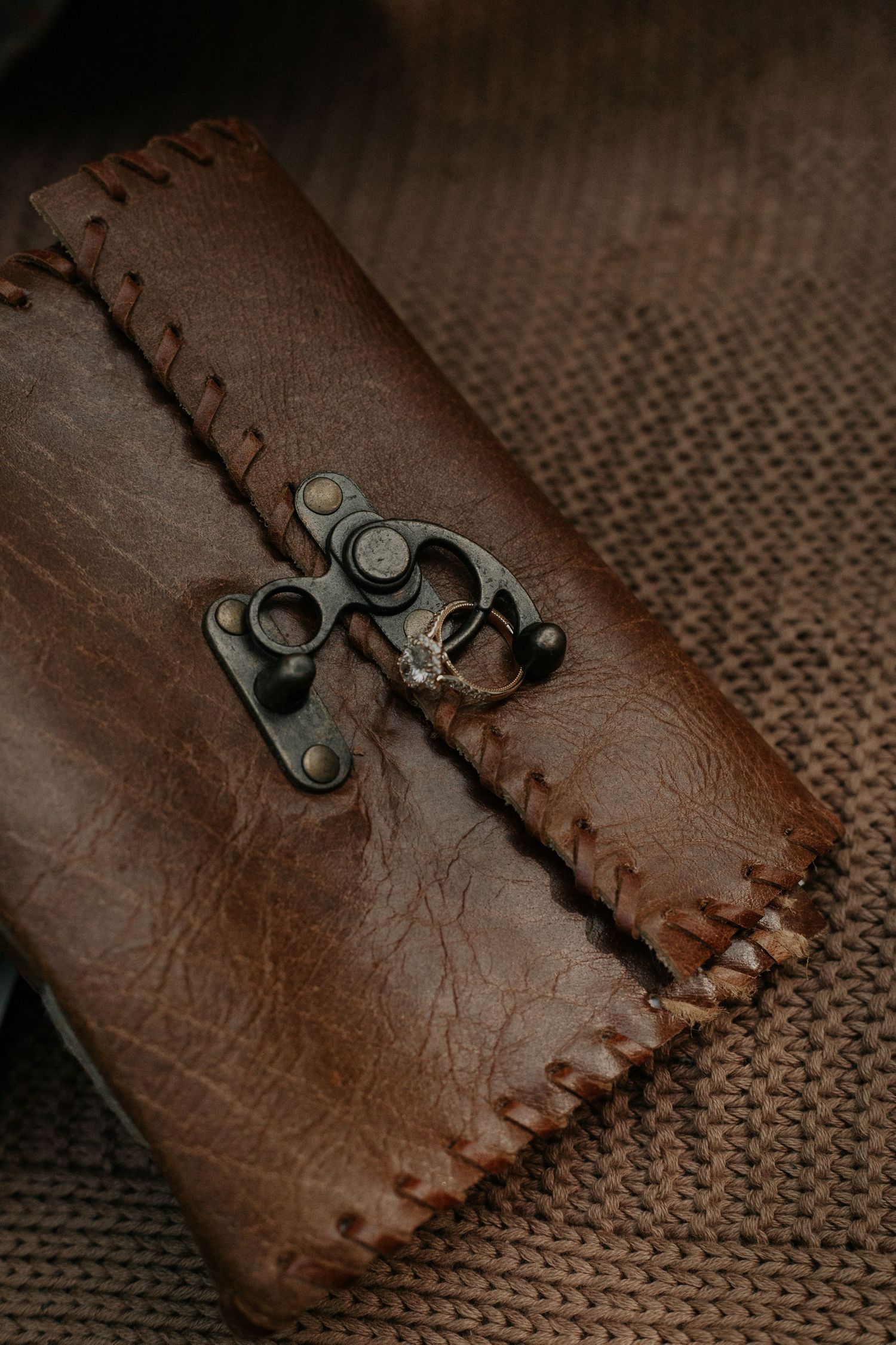 Close-up of a rustic brown leather journal with antique metal clasp and delicate rings on burlap.