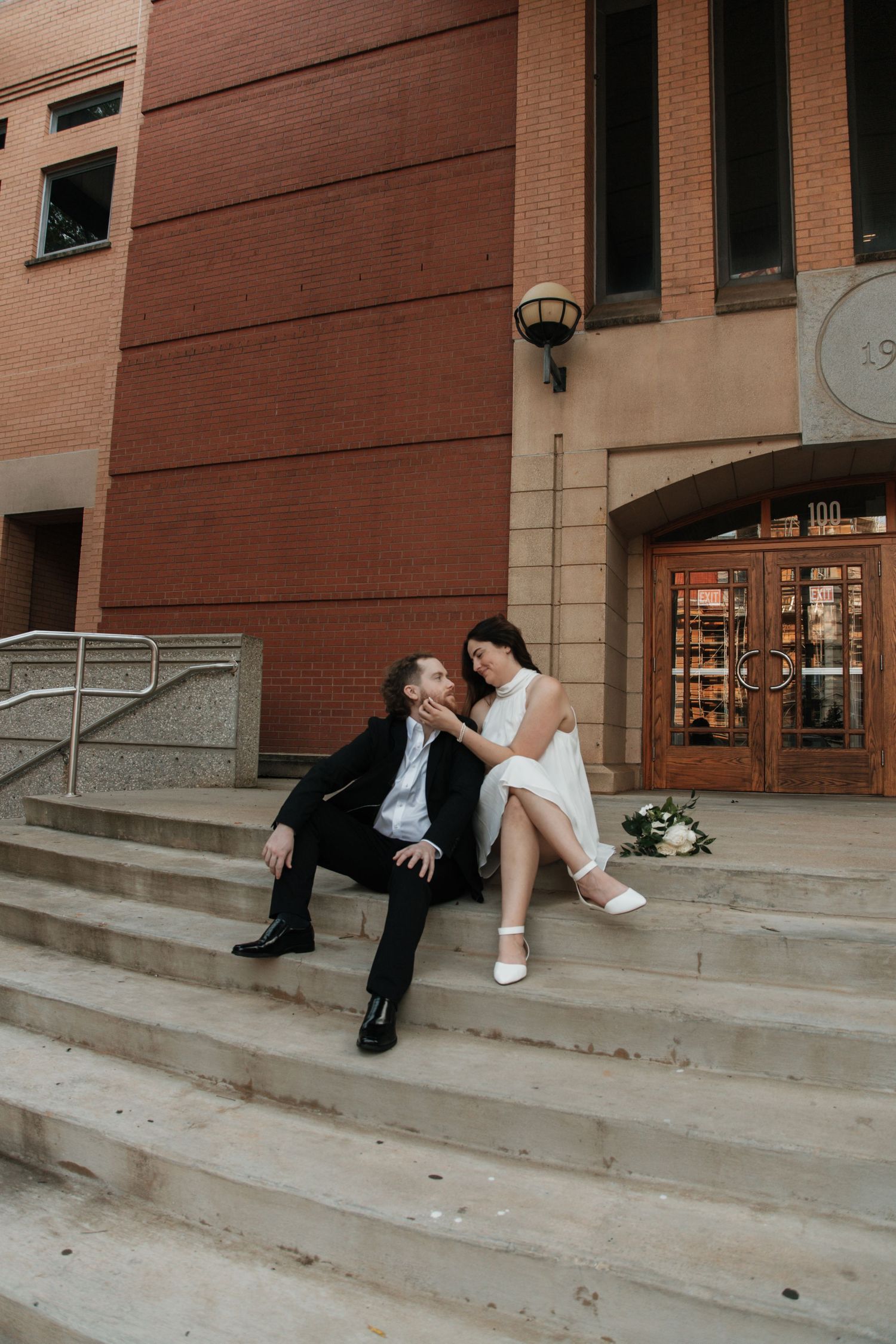Newlyweds sitting on stone steps of brick building, sharing romantic moment on wedding day. anderson court house sc