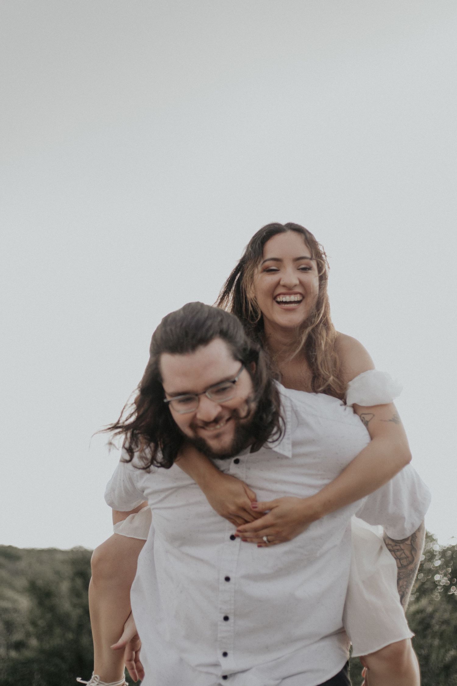 Joyful couple sharing a piggyback ride against an open sky backdrop.