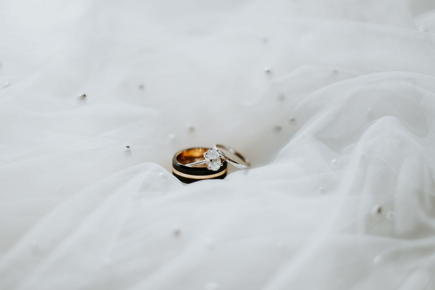 Gold wedding band and diamond engagement ring resting on white bridal veil.