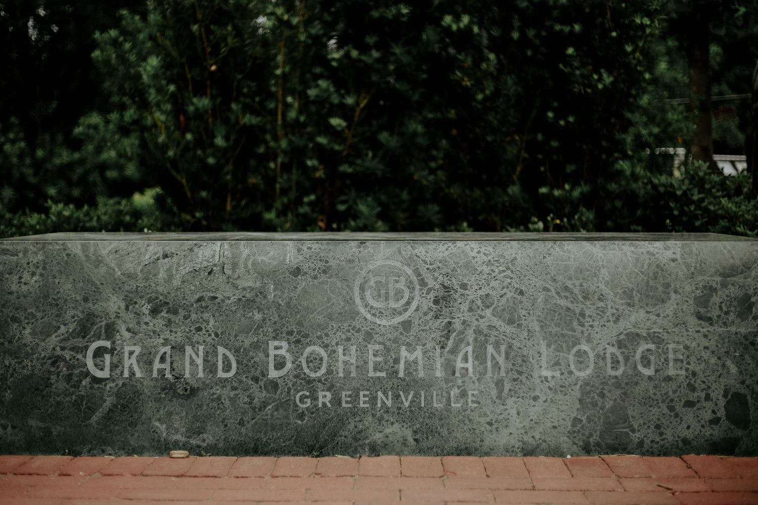 Stone entrance sign for Grand Bohemian Lodge Greenville surrounded by lush green trees.