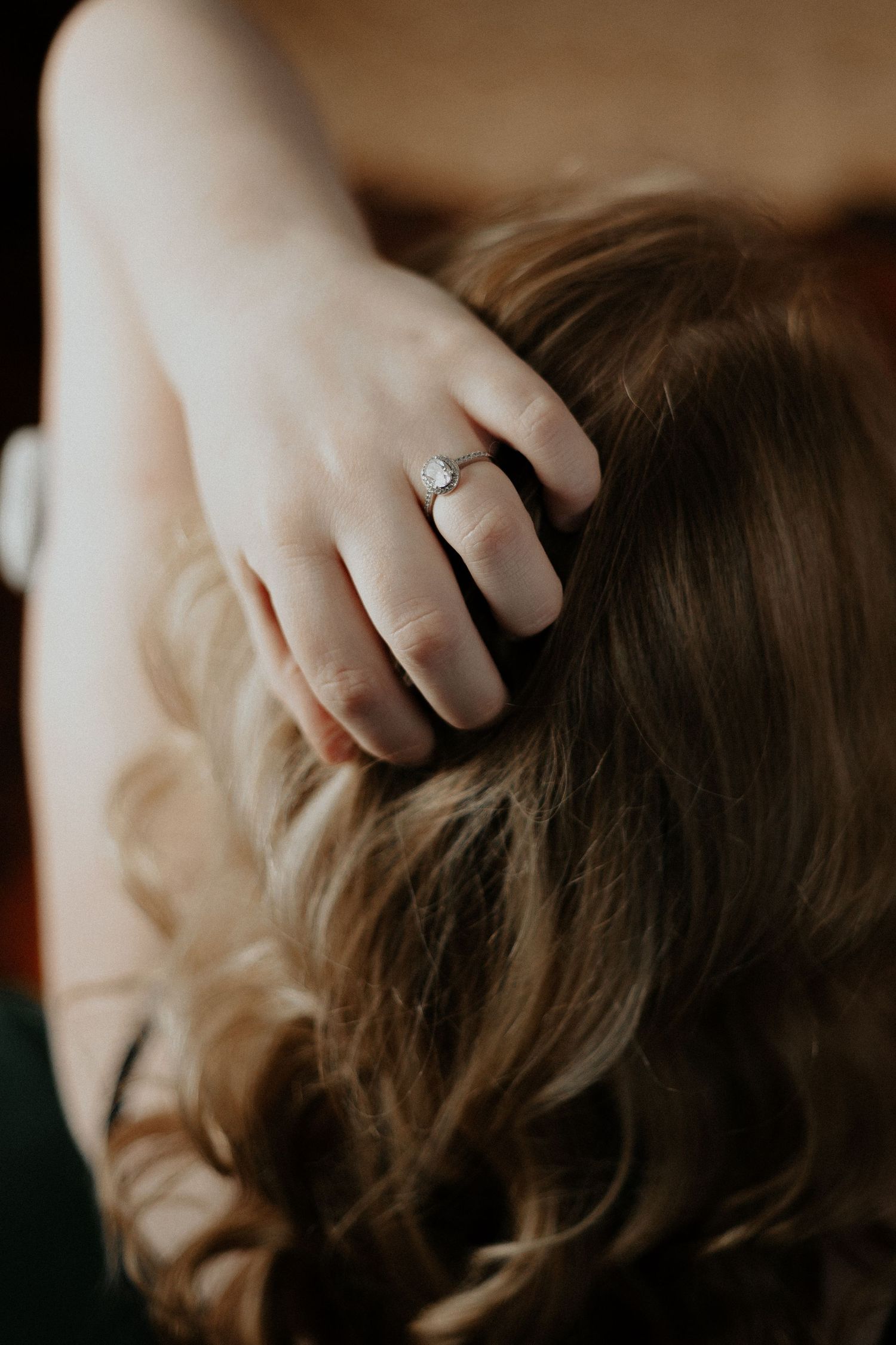 Close-up of a diamond engagement ring on a woman's finger resting in her wavy hair.