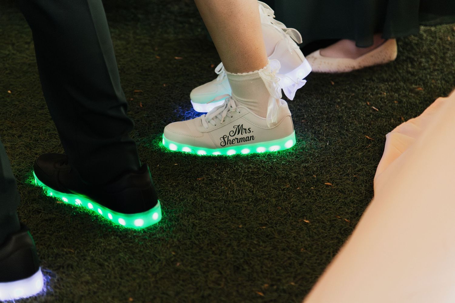 Bride and groom wearing light-up LED wedding sneakers, with Mrs. written on the white high-top shoes.