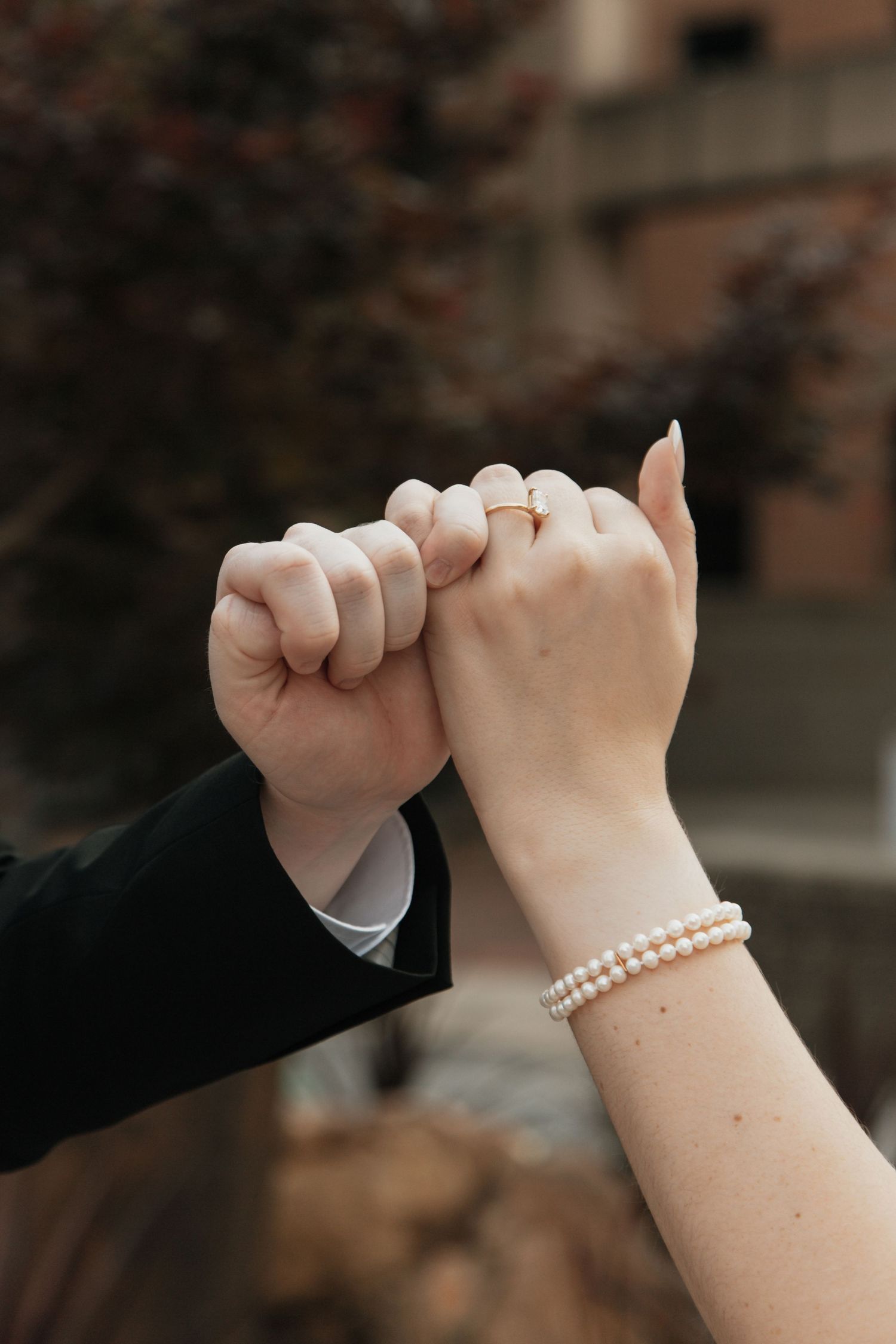 Close-up of newlyweds linking pinky fingers, bride wearing pearl bracelet and diamond ring.
