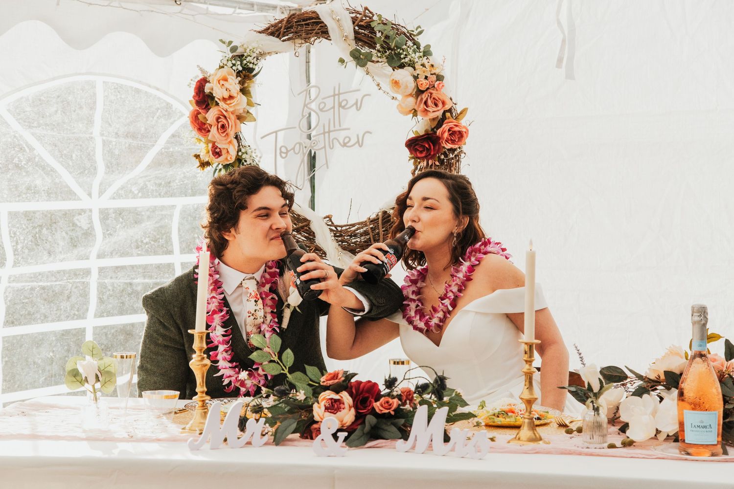 Bride and groom sharing a microphone at wedding reception table decorated with tropical floral arrangements.