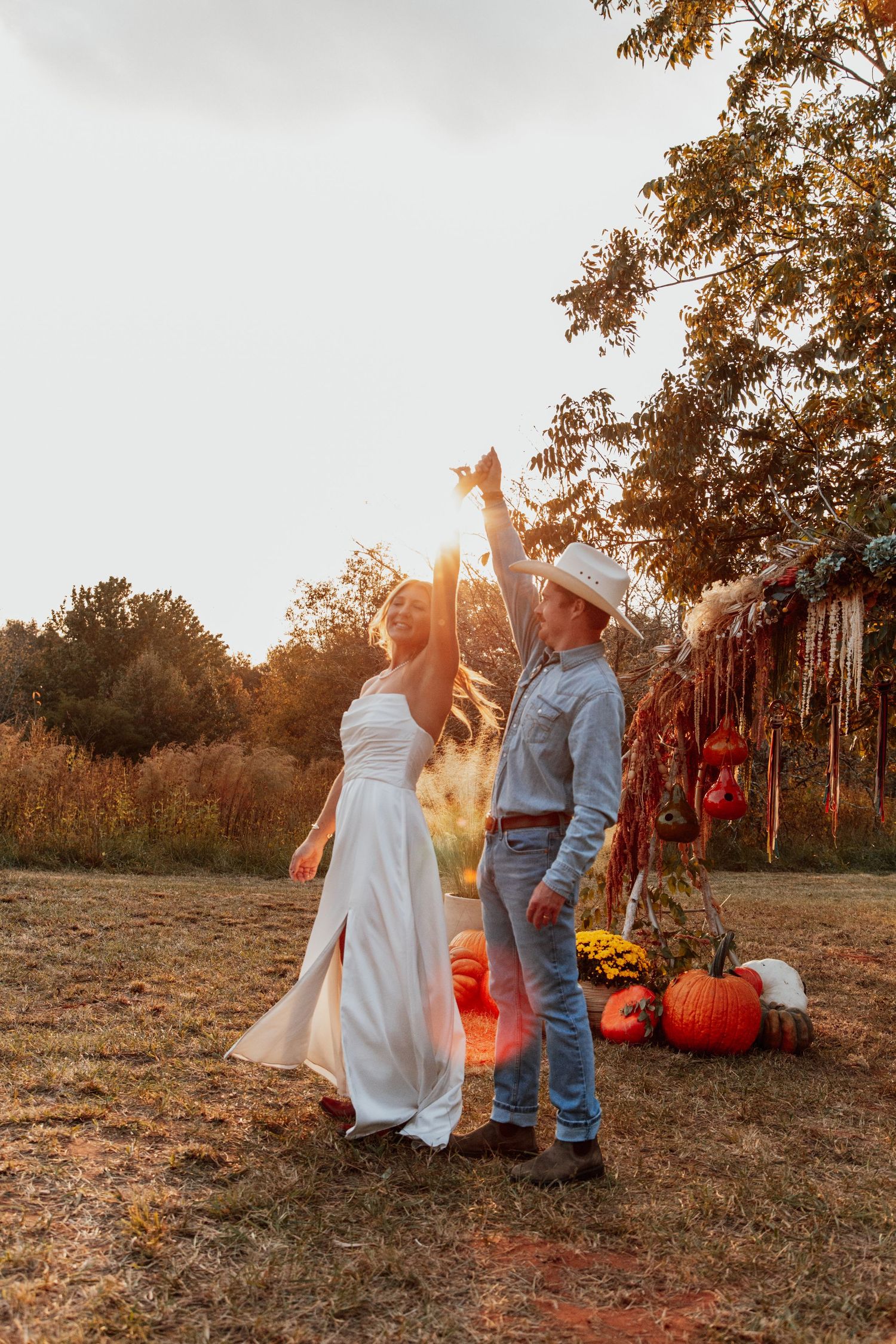 Couple dancing outdoors at a fall wedding with pumpkins and autumn foliage in golden sunset light.