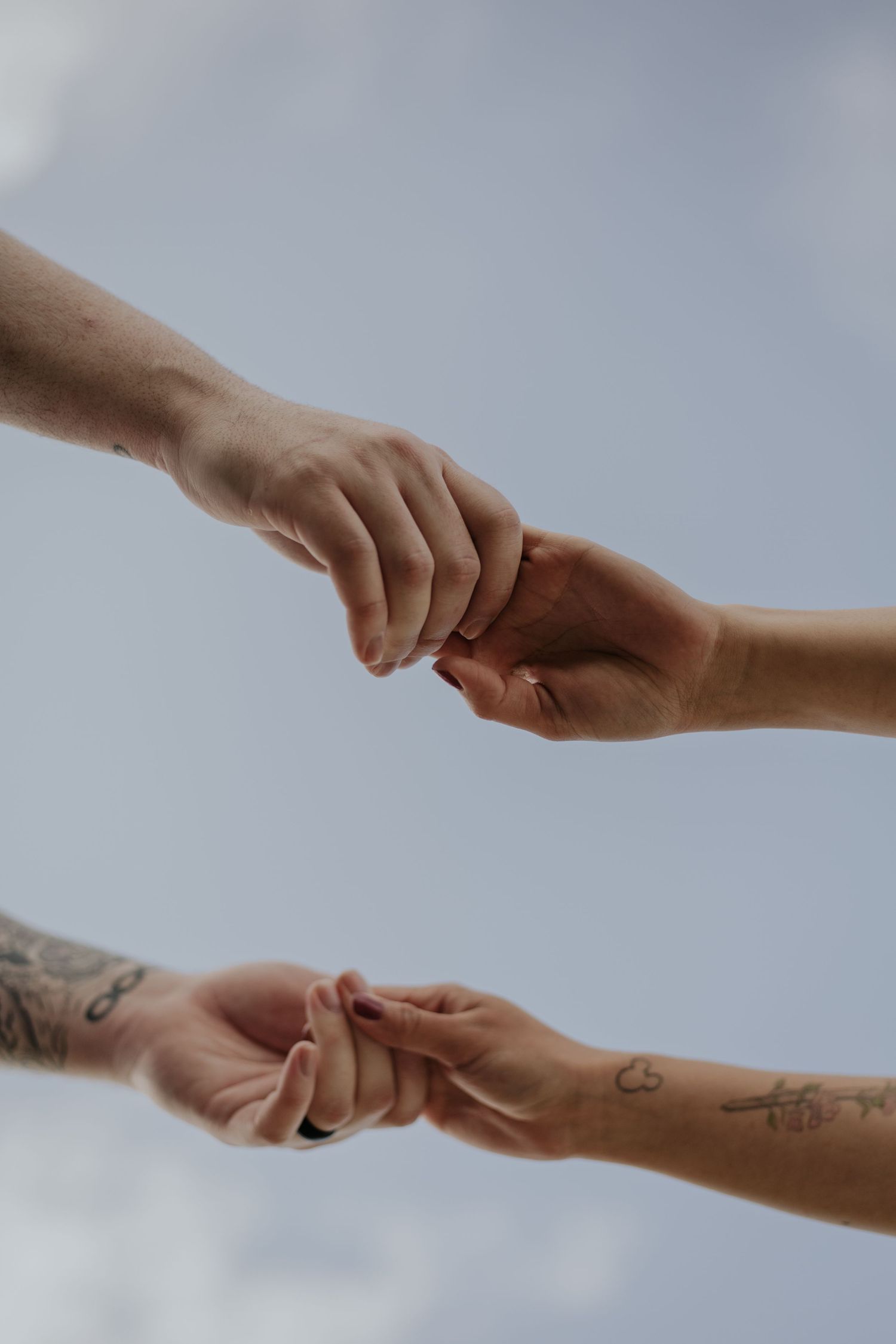Two pairs of hands reaching toward each other against a cloudy sky.