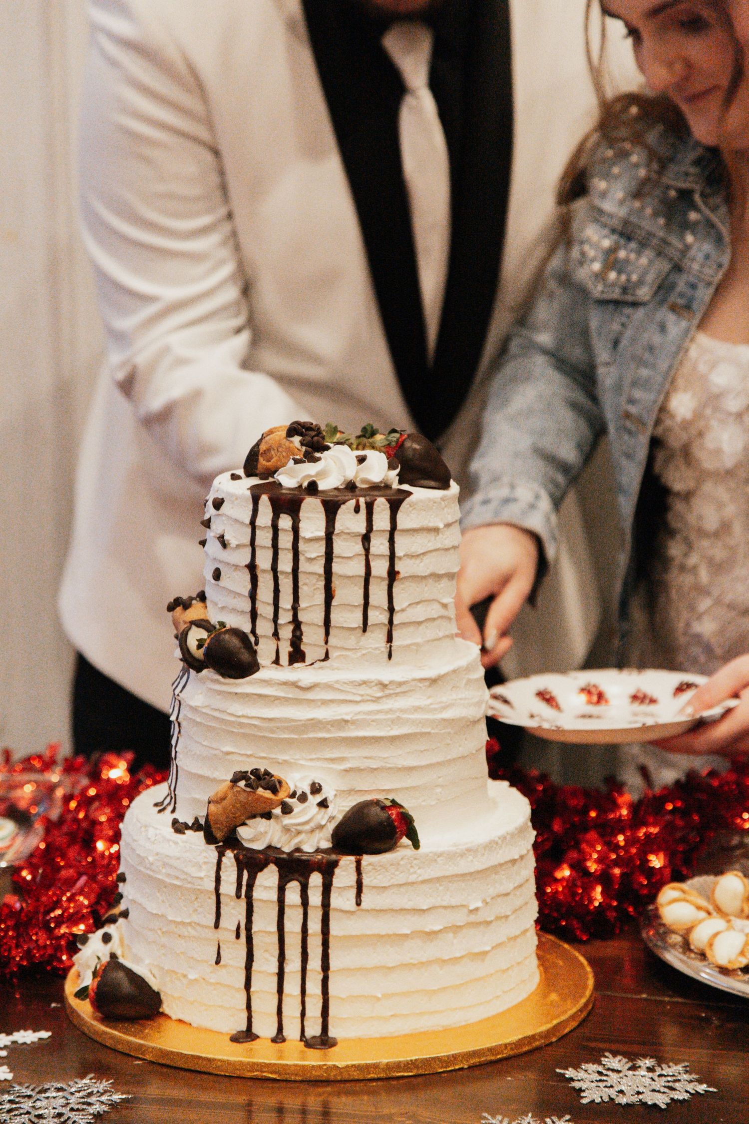 Bride and groom cutting their three-tier white wedding cake adorned with chocolate-covered strawberries and chocolate drizzle.