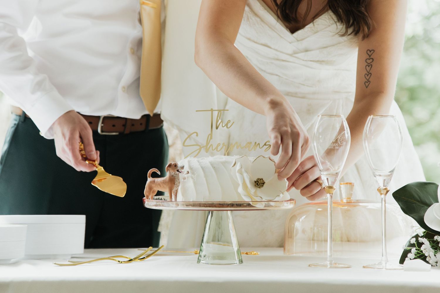 Newlyweds cut elegant white wedding cake together at reception table with gold cake topper.