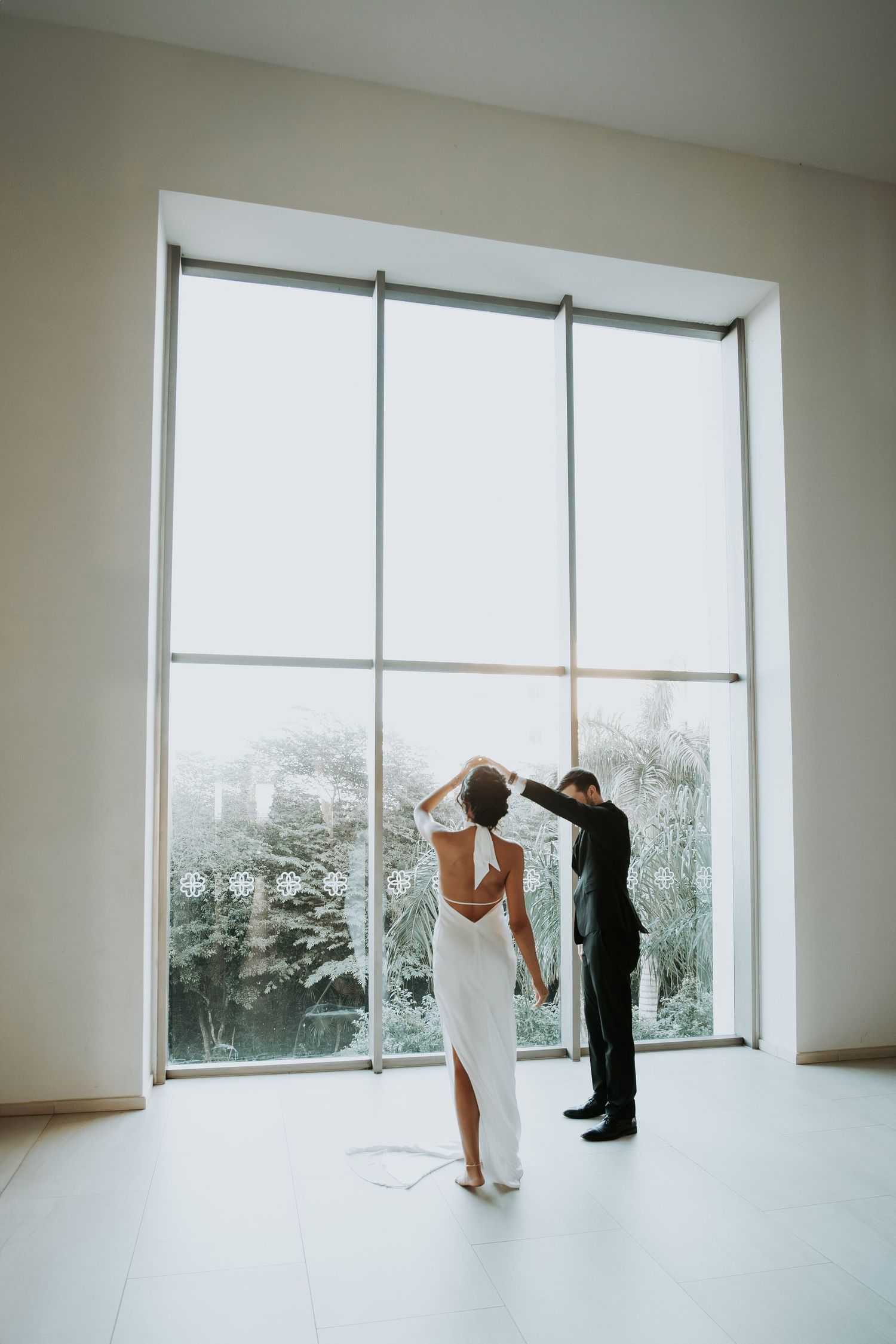 Bride and groom stand before a large floor-to-ceiling window in a bright modern venue. - riviera maya resort (cancun, Mexico)