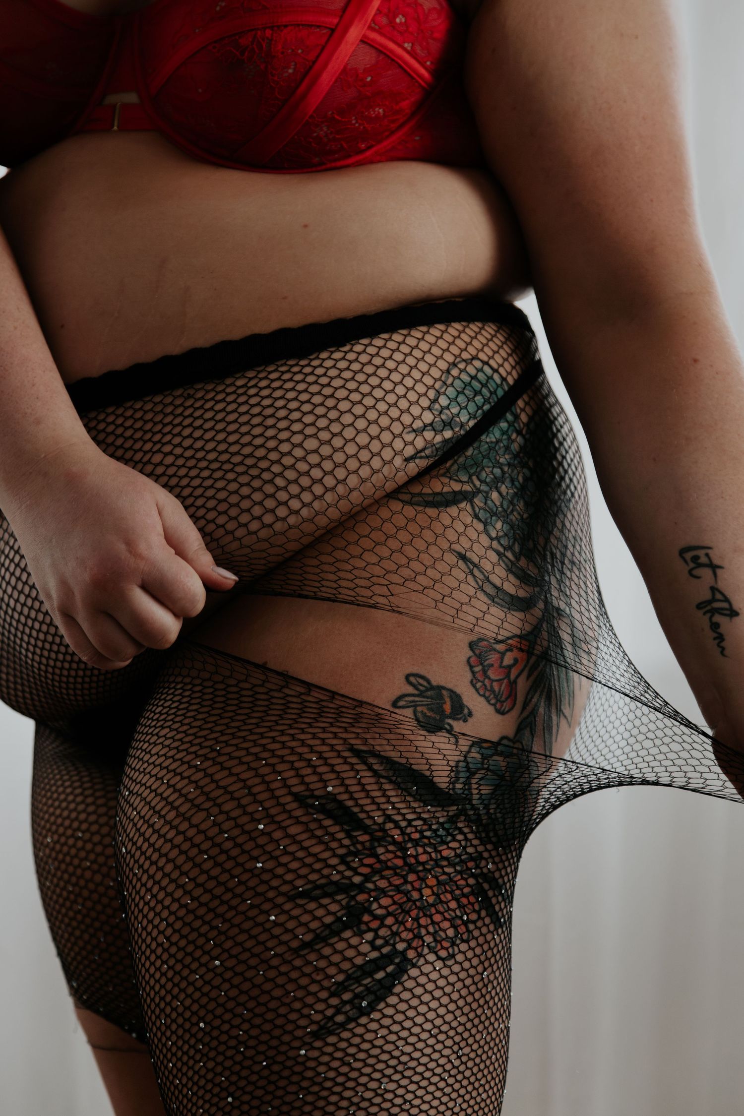 Woman in red lingerie and black fishnet tights with floral tattoos posing for boudoir photography.. wanderlust boudoir studio honea path sc
