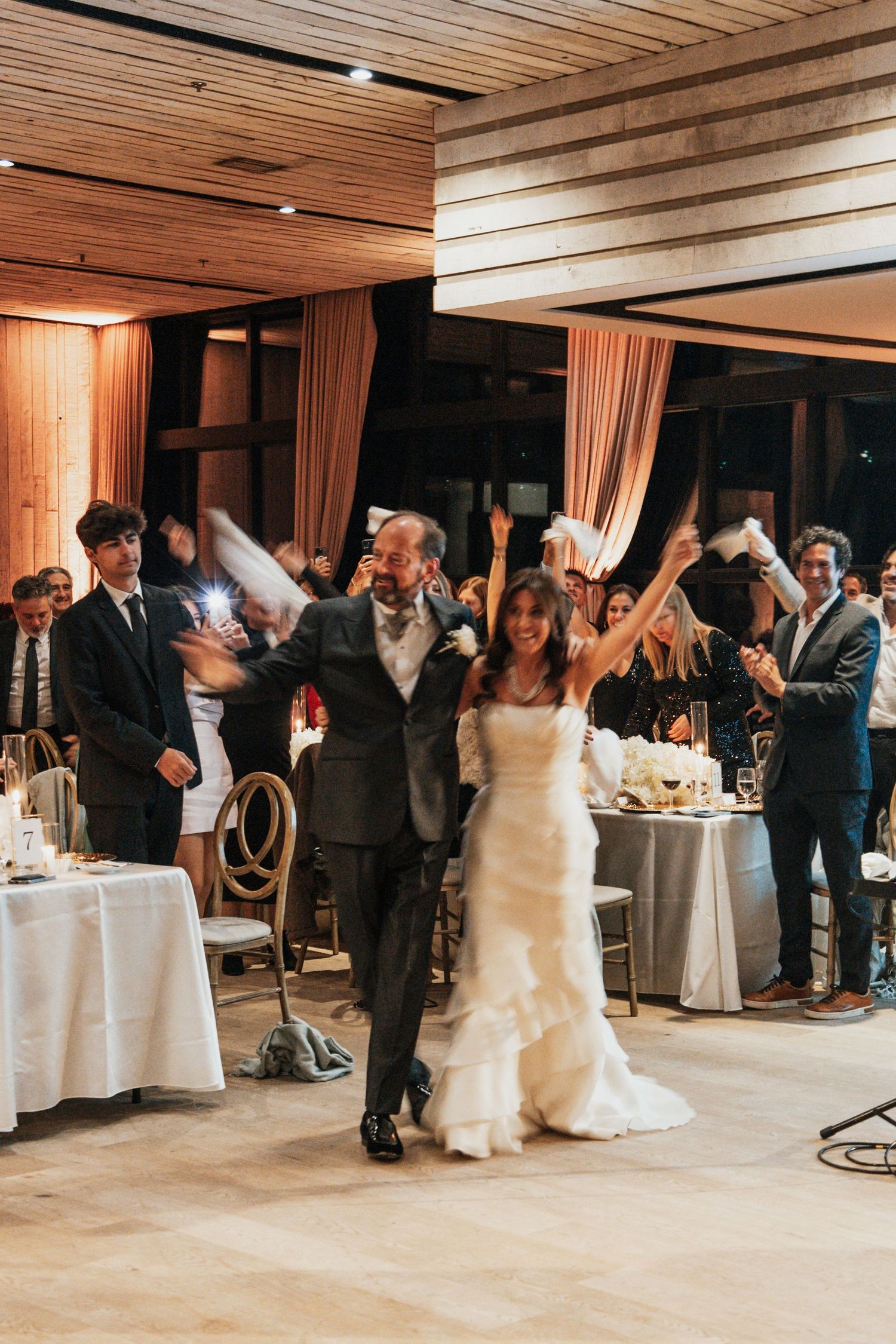 Bride and groom making grand entrance into wedding reception as guests cheer and wave napkins in celebration. middleton place sc