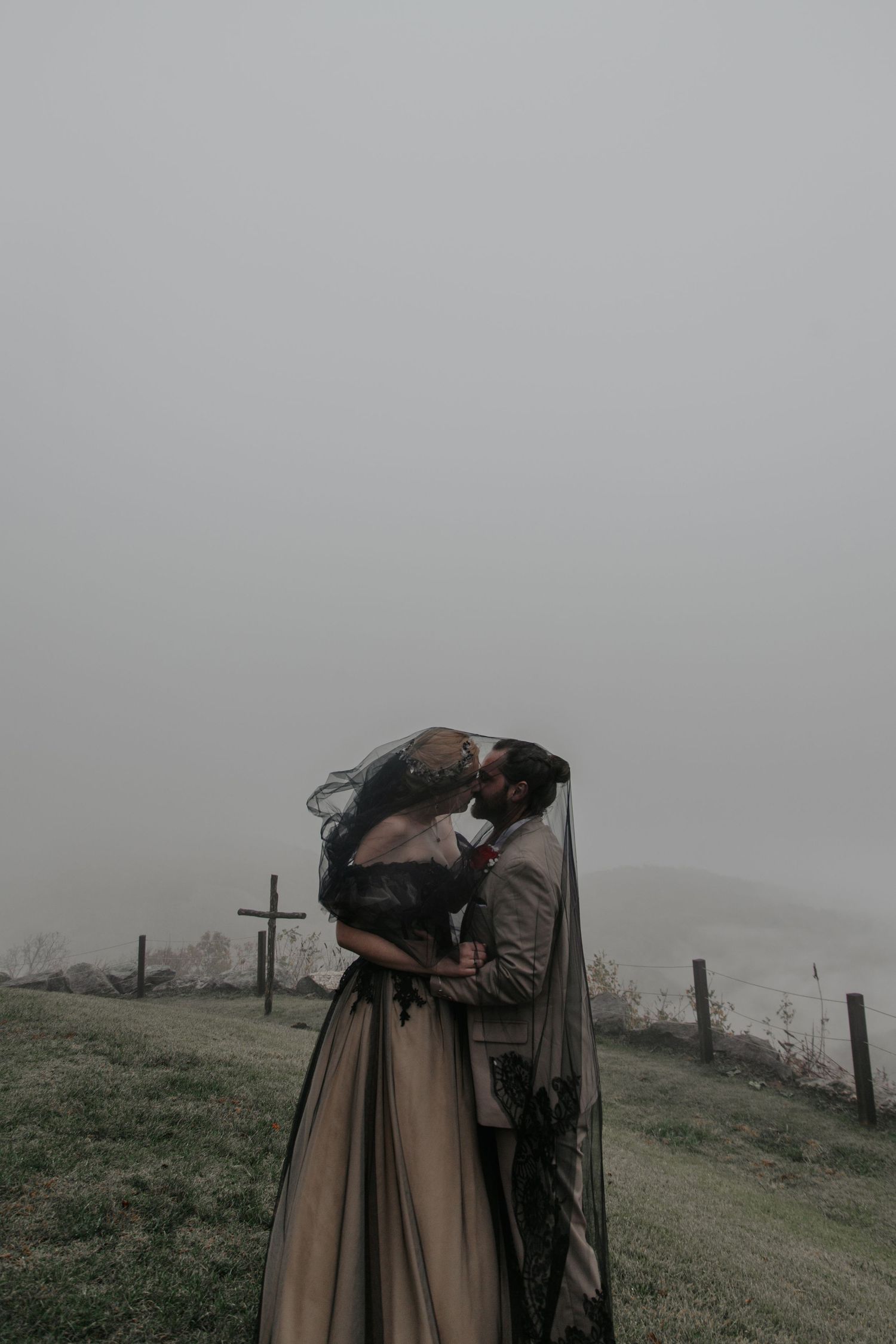 Couple sharing a romantic kiss in misty foggy landscape, bride in black gothic wedding gown with veil.- Glassy Mountain Chapel (landrum, sc)