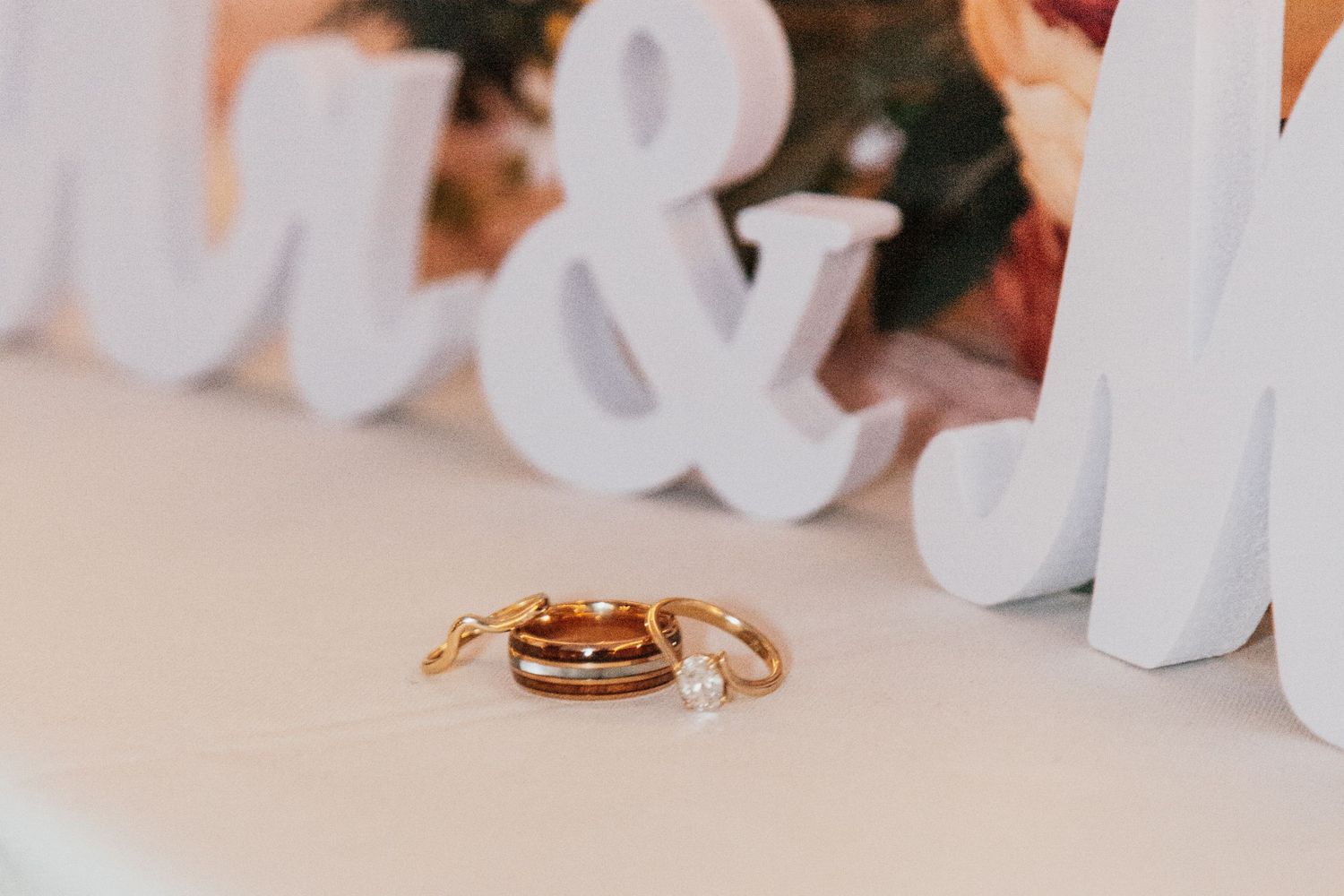 Gold wedding rings and diamond engagement ring displayed on white table with decorative Mr and Mrs letters.