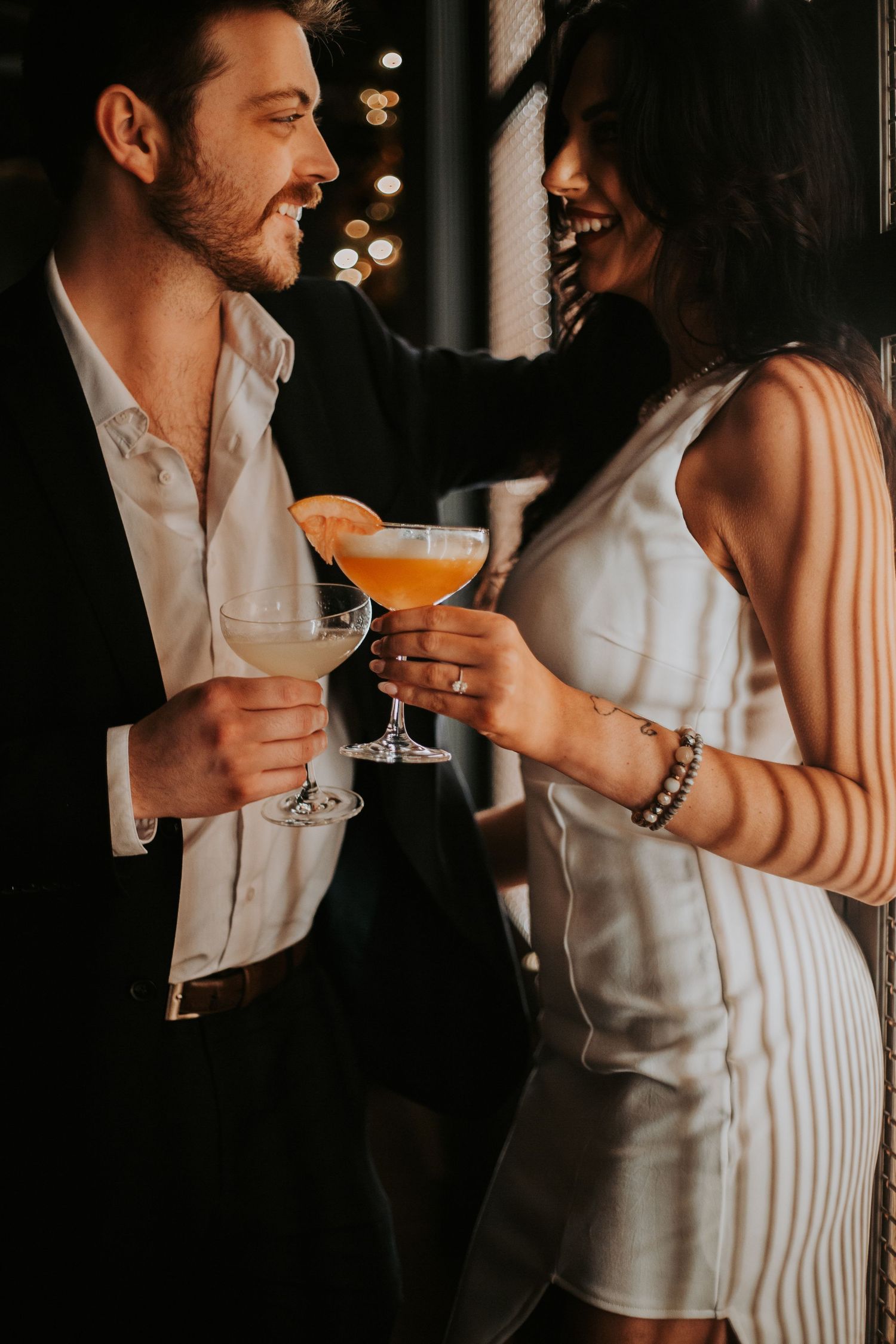Couple laughing and toasting with cocktails in a dimly lit elegant bar setting. grand bohemian lodge greenville sc