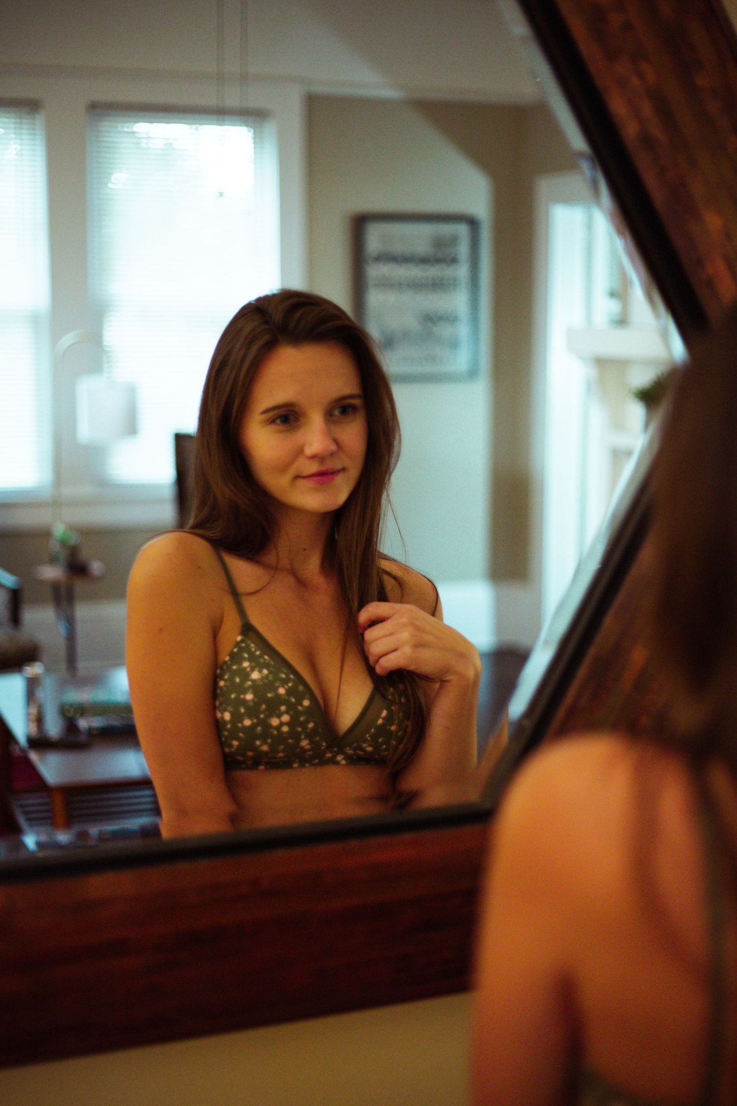 Young woman in olive green bikini top posing in front of a mirror indoors.