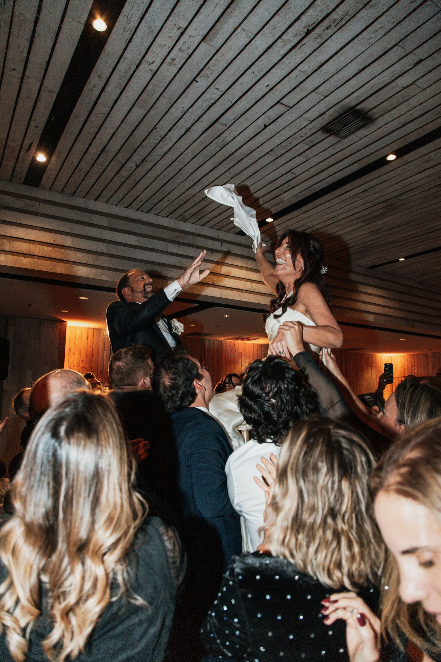 Bride being lifted by wedding guests during lively reception dance floor celebration at indoor venue middleton place sc