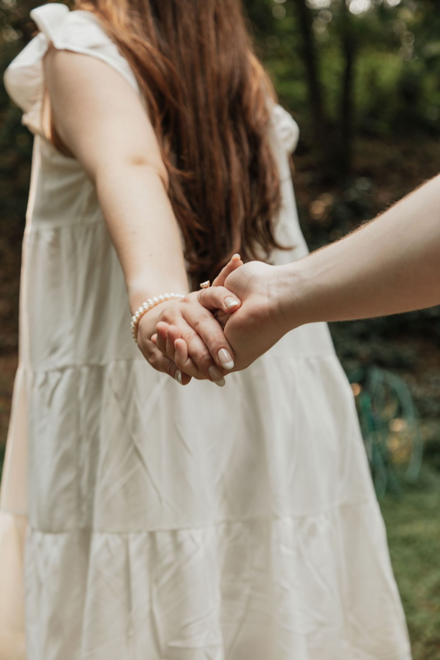 Close-up of couple holding hands with woman wearing pearl bracelet in white summer dress.