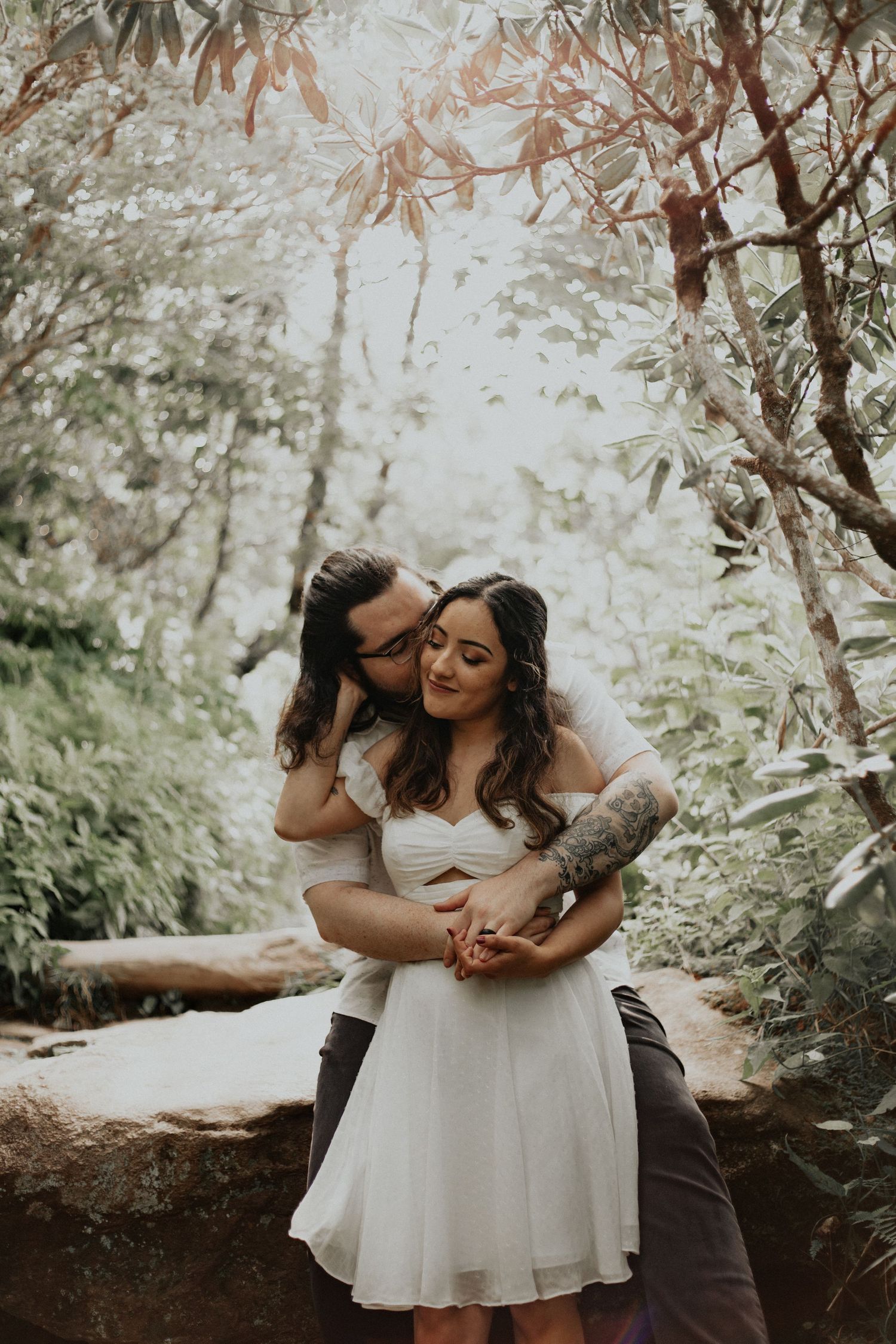 Couple sharing a romantic moment on a rock in a misty forest.