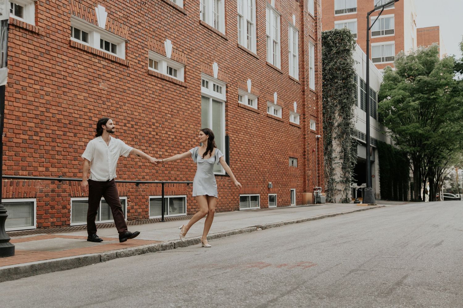 Couple holding hands walking along a brick building street in a romantic urban setting.