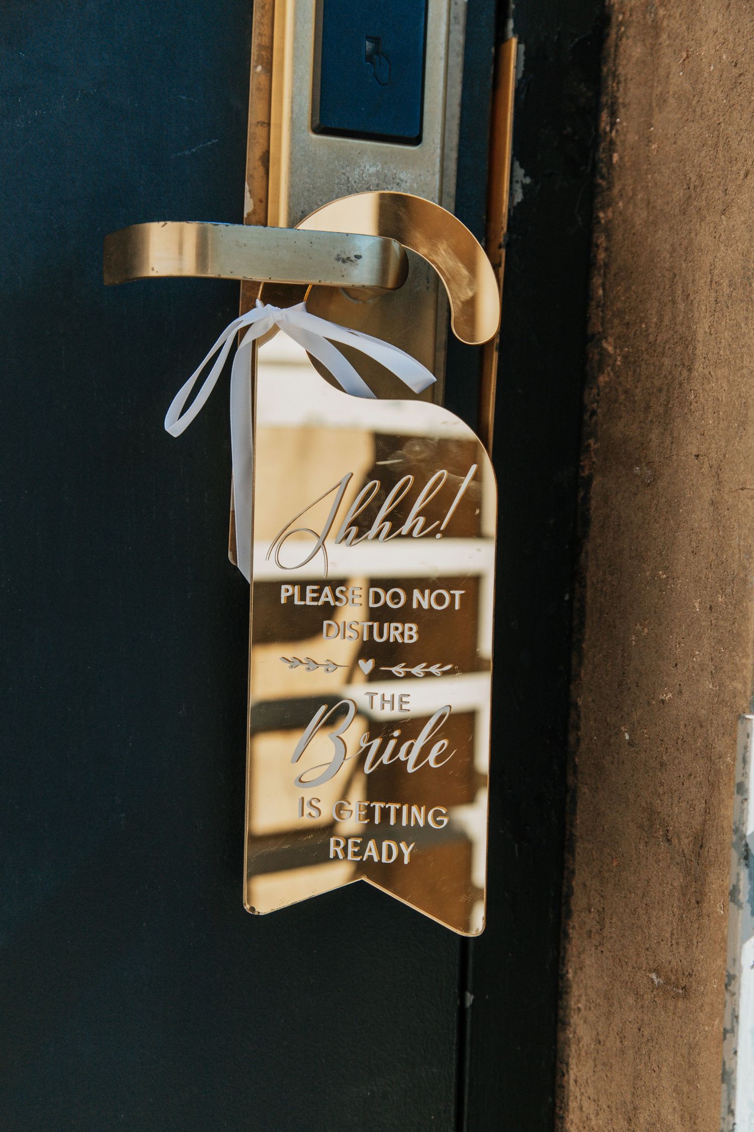 Gold do not disturb door hanger sign reading Shhh, the bride is getting ready, tied with white ribbon.