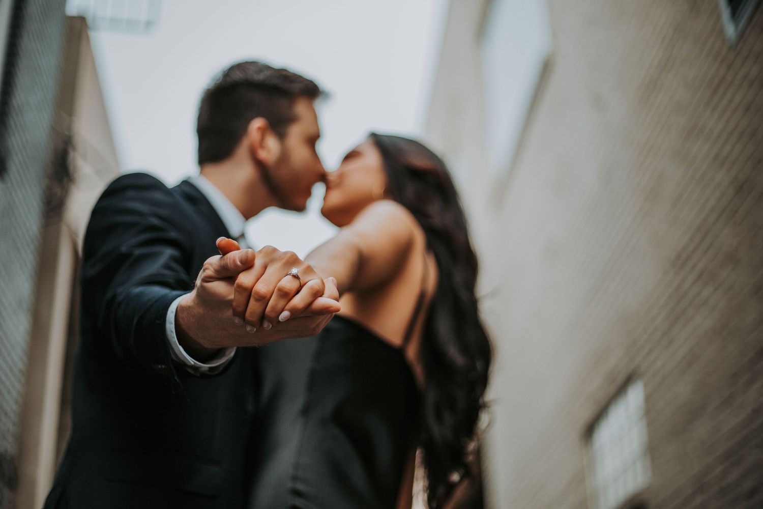 Engaged couple kissing in an alley while holding hands and showing off their ring. greenville sc