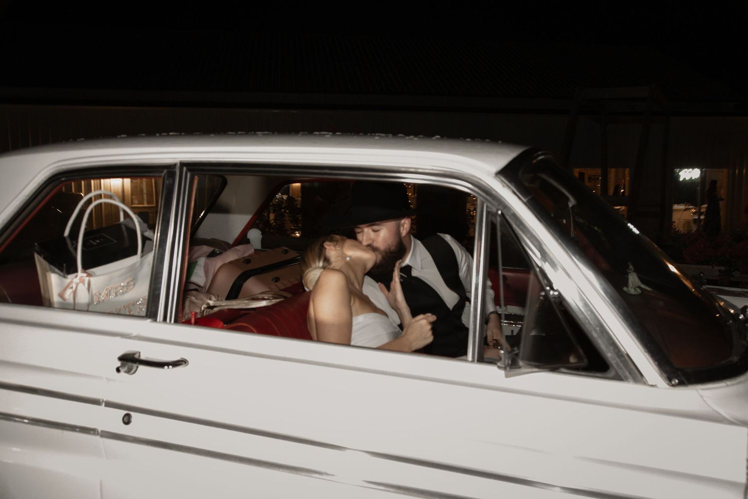 Newlyweds share a kiss inside a classic vintage white car during their wedding night getaway. Roger's Farm Buffalo SC.