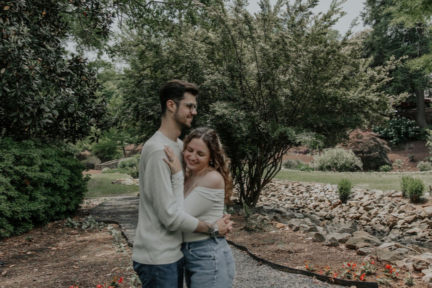 Couple embracing warmly in a lush garden setting during a relaxed outdoor engagement photo session. rock quarry garden greenville sc