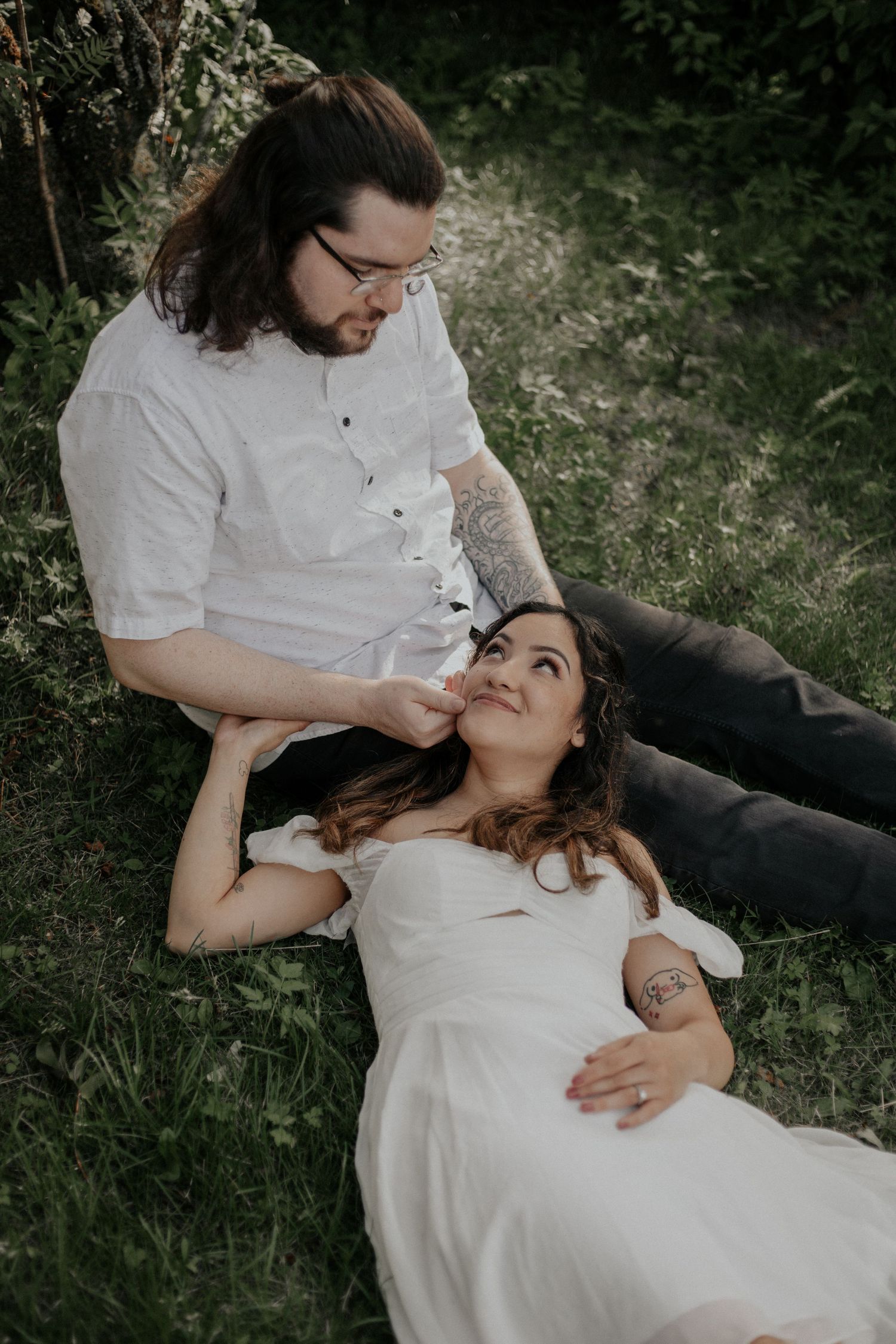 Couple relaxing in lush green grass as groom gazes at smiling bride.