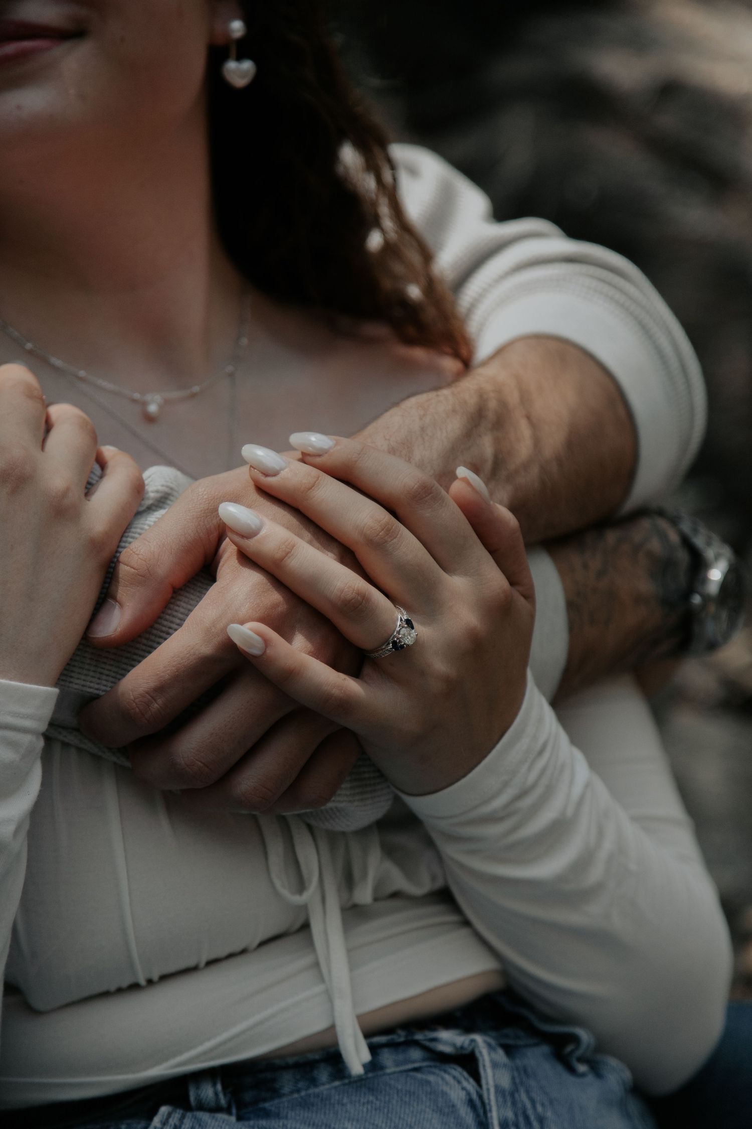 Close-up of couple holding hands showing engagement ring and tattoos.