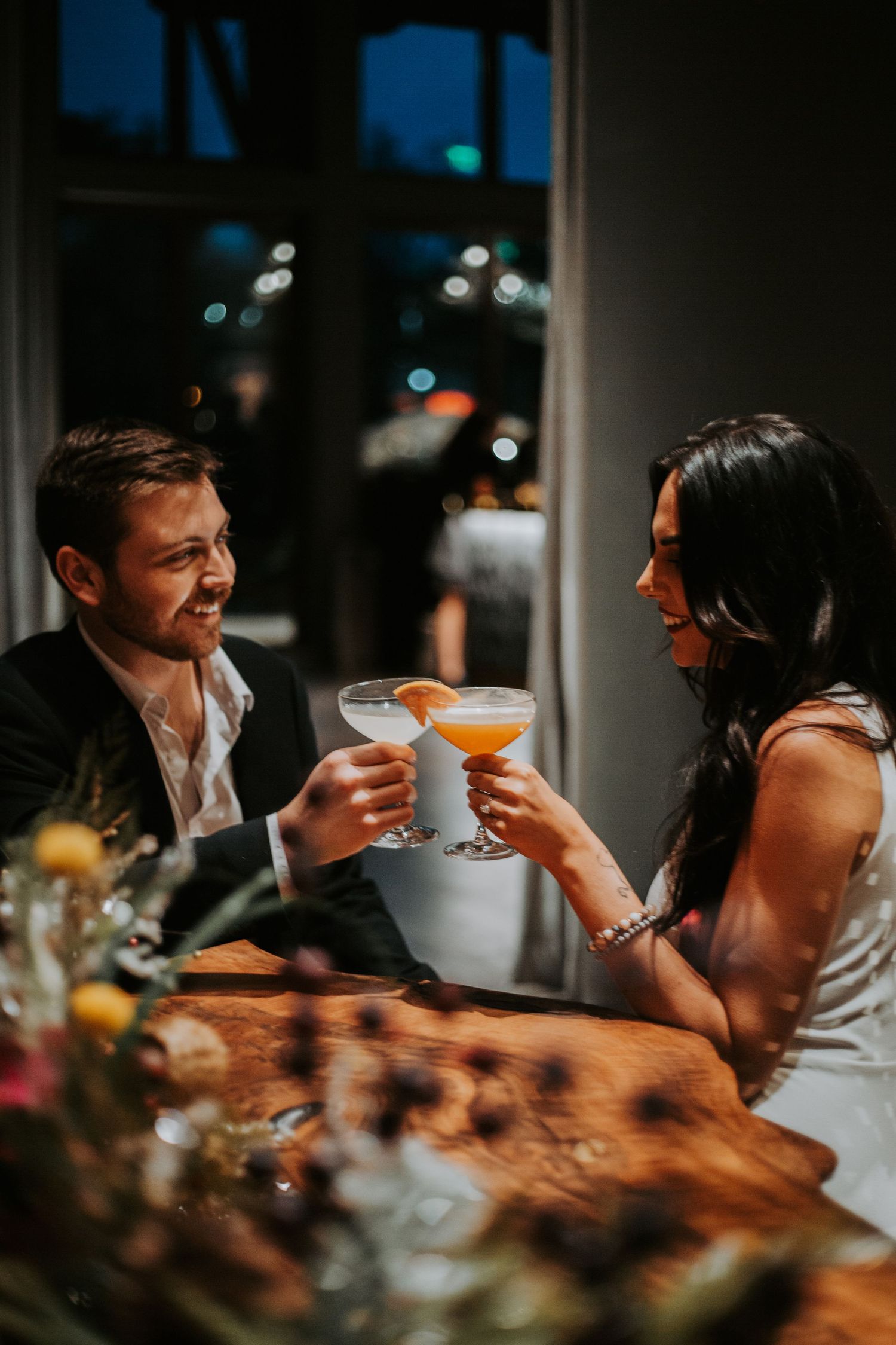 Couple toasting cocktails at romantic candlelit dinner table, celebrating special occasion at elegant restaurant.