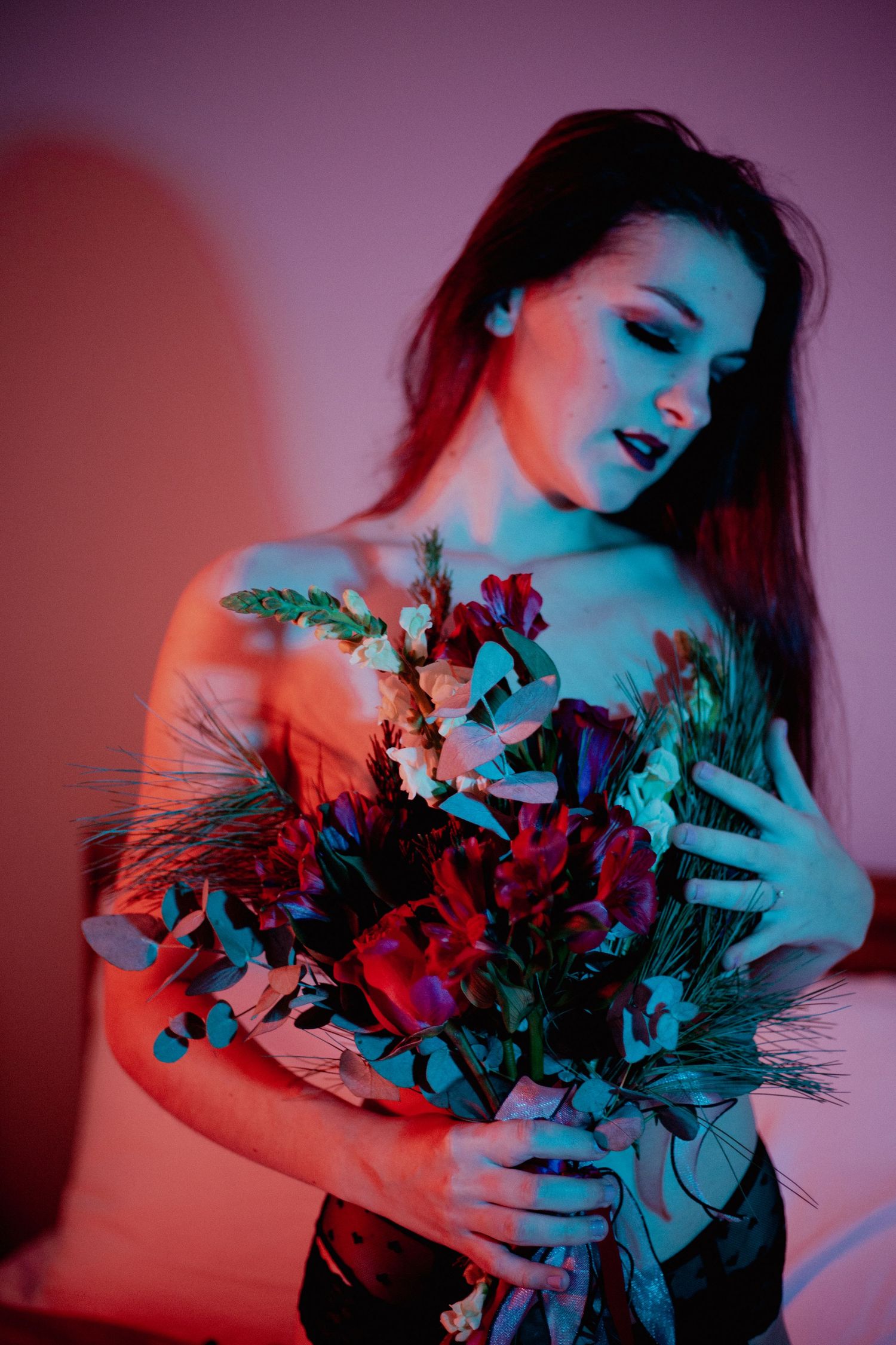 A dark-haired woman holds a lush floral bouquet under dramatic red and blue neon lighting indoors.