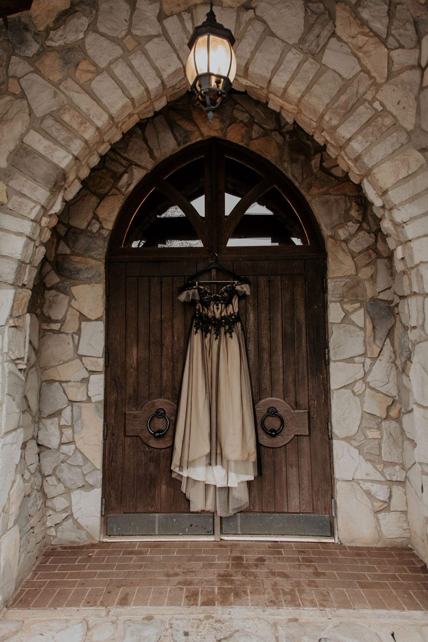 An elegant black and champagne wedding gown hangs on a Gothic stone arched wooden chapel door.- Glassy Mountain Chapel (landrum, sc)