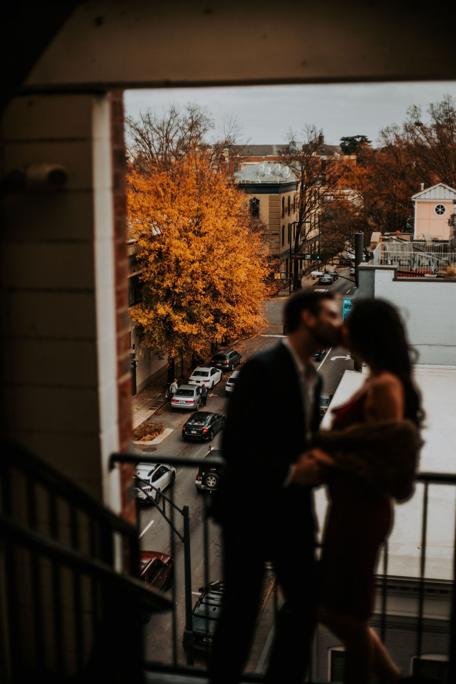 Couple sharing a kiss on a balcony overlooking a city street with autumn foliage. downtown greenville sc