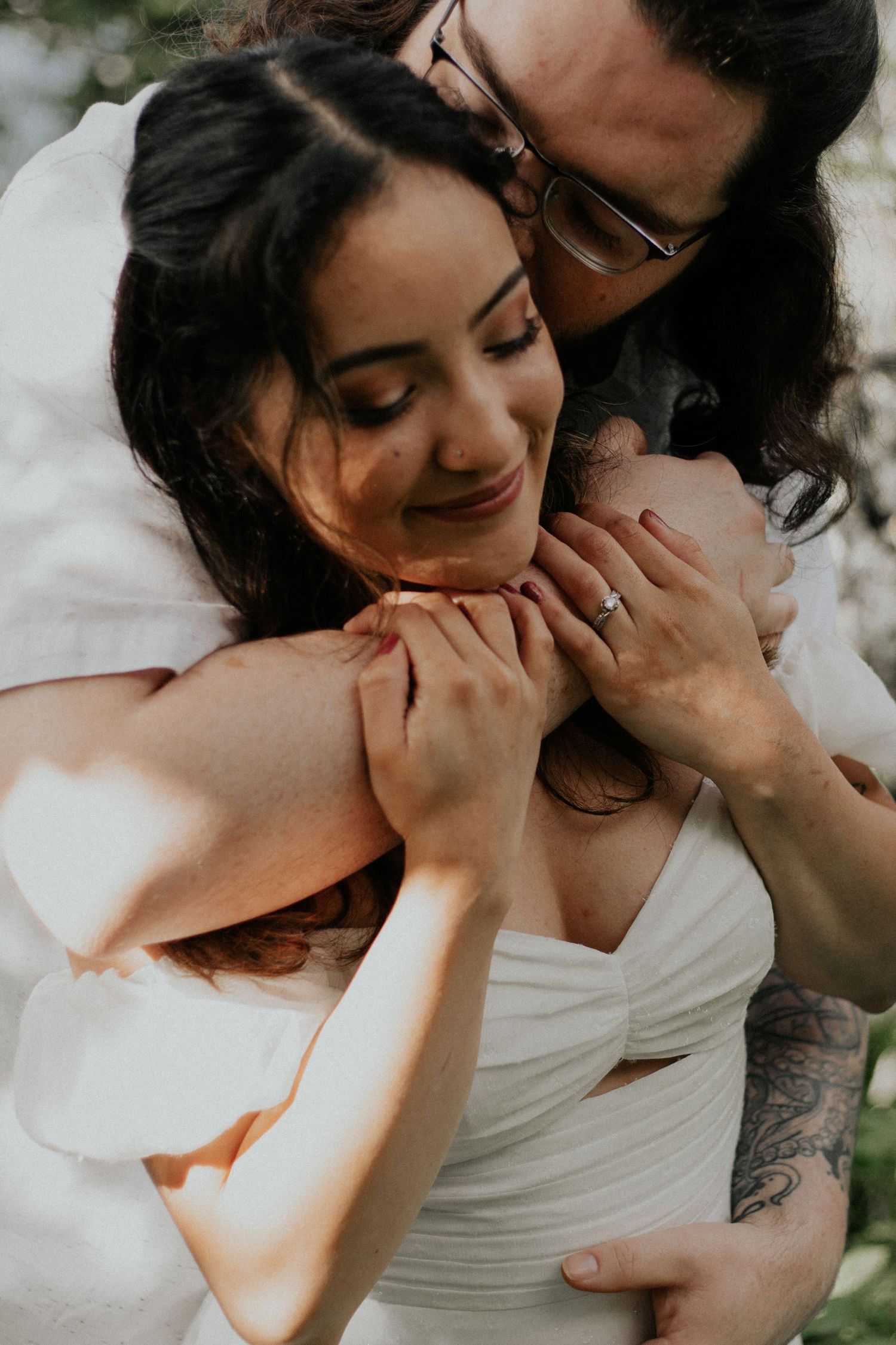 Groom tenderly embraces bride from behind in warm golden light.