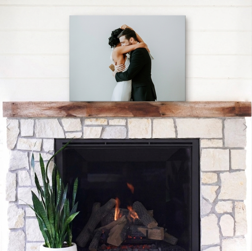 A wedding photo canvas print displayed on a rustic wood mantel above a stone fireplace with a cozy fire burning.