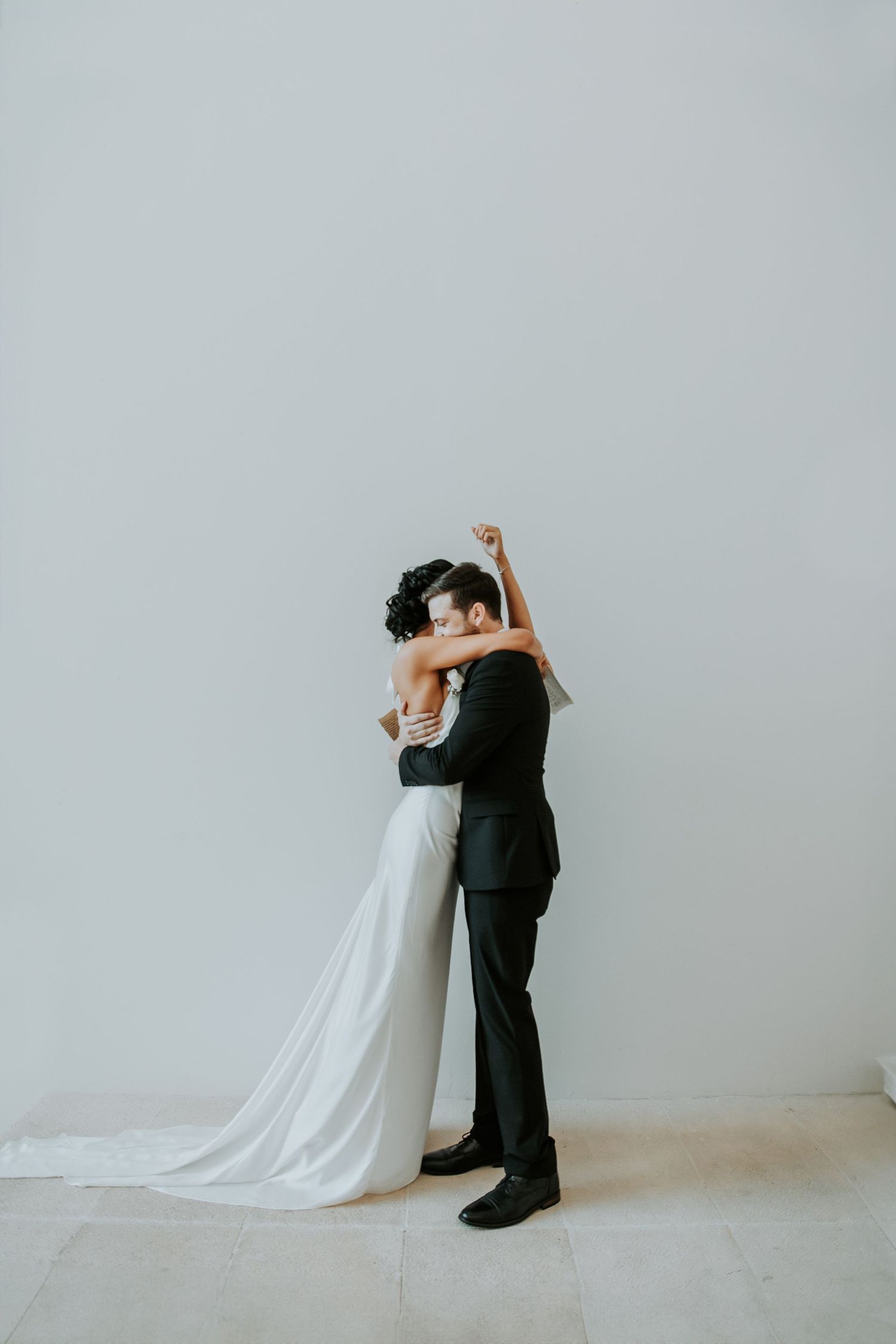 Bride and groom share a tender embrace against a clean white minimalist wall. - riviera maya resort (cancun, Mexico)