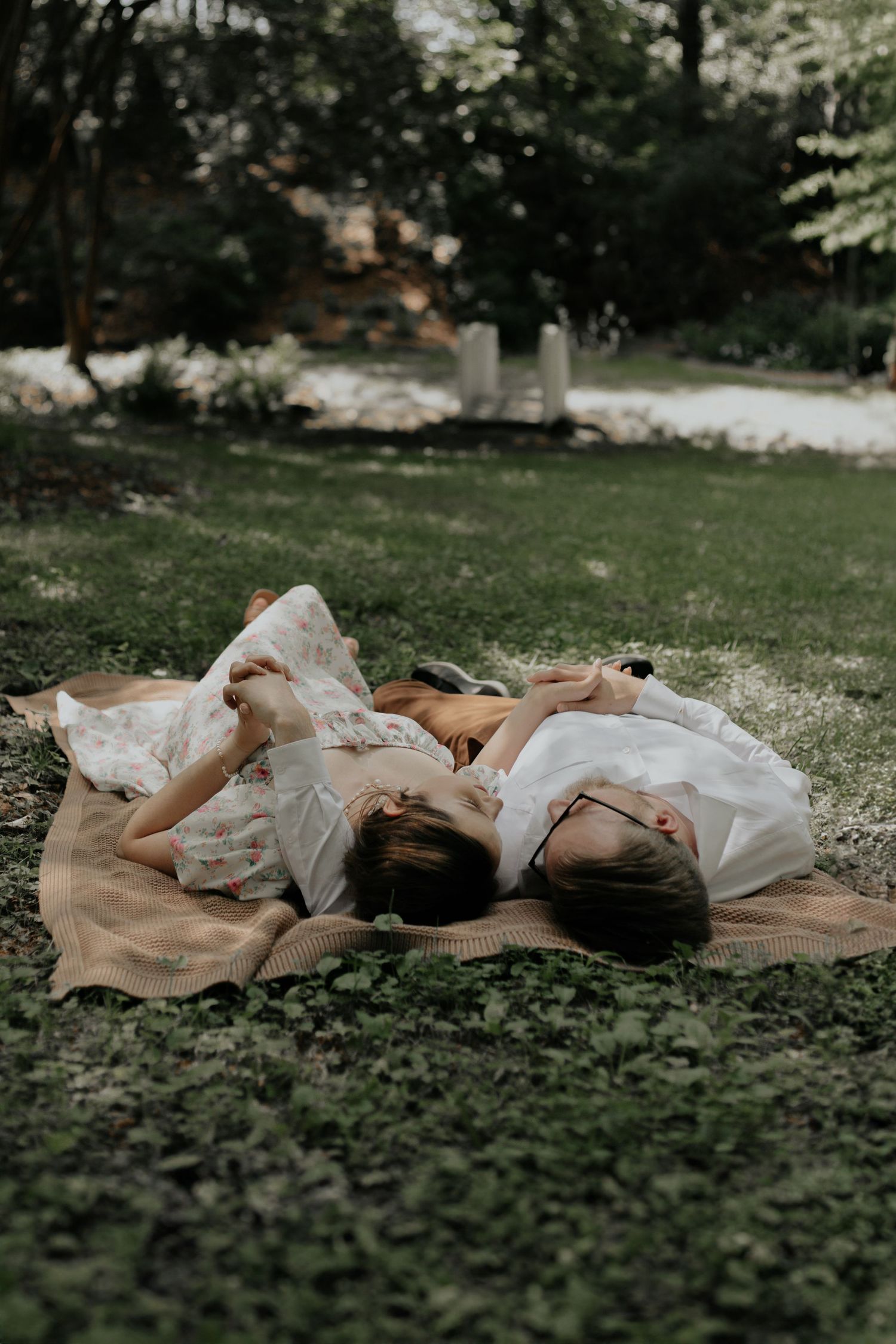 Two women in floral dresses lying on blanket in lush green garden setting. kilgore lewis house greenville sc
