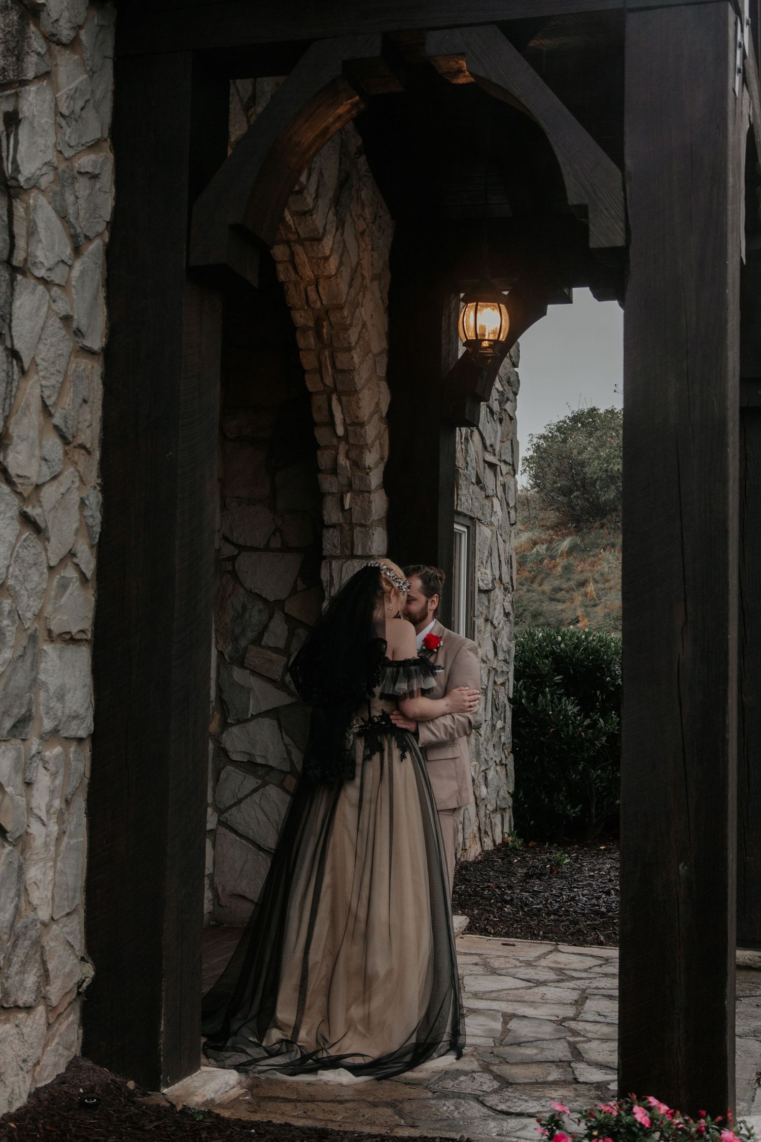 A couple shares a romantic kiss under a stone Gothic arch at their wedding venue at dusk.- Glassy Mountain Chapel (landrum, sc)