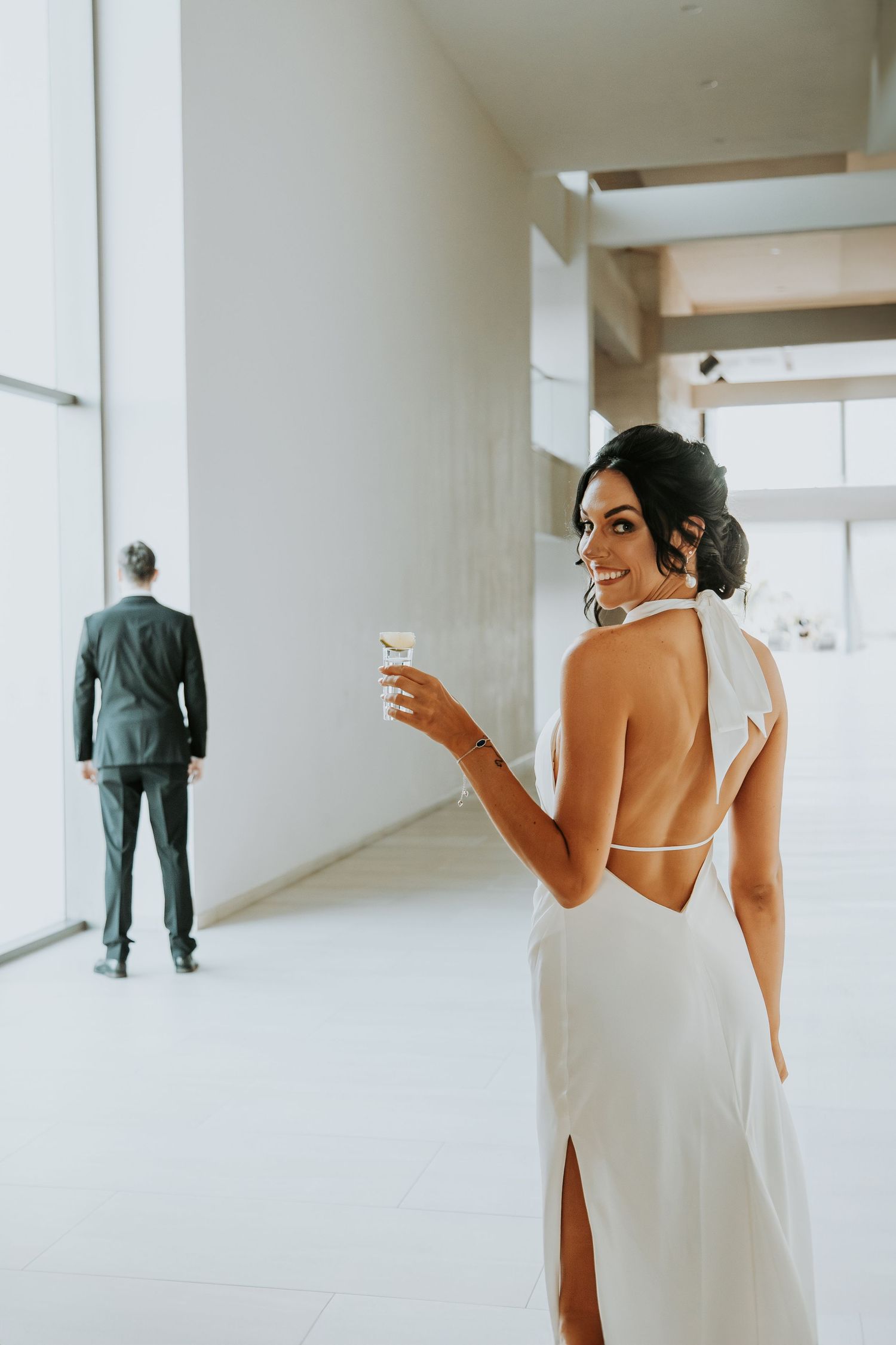 Smiling bride in backless white halter gown holds champagne glass at elegant modern wedding venue. - riviera maya resort (cancun, Mexico)