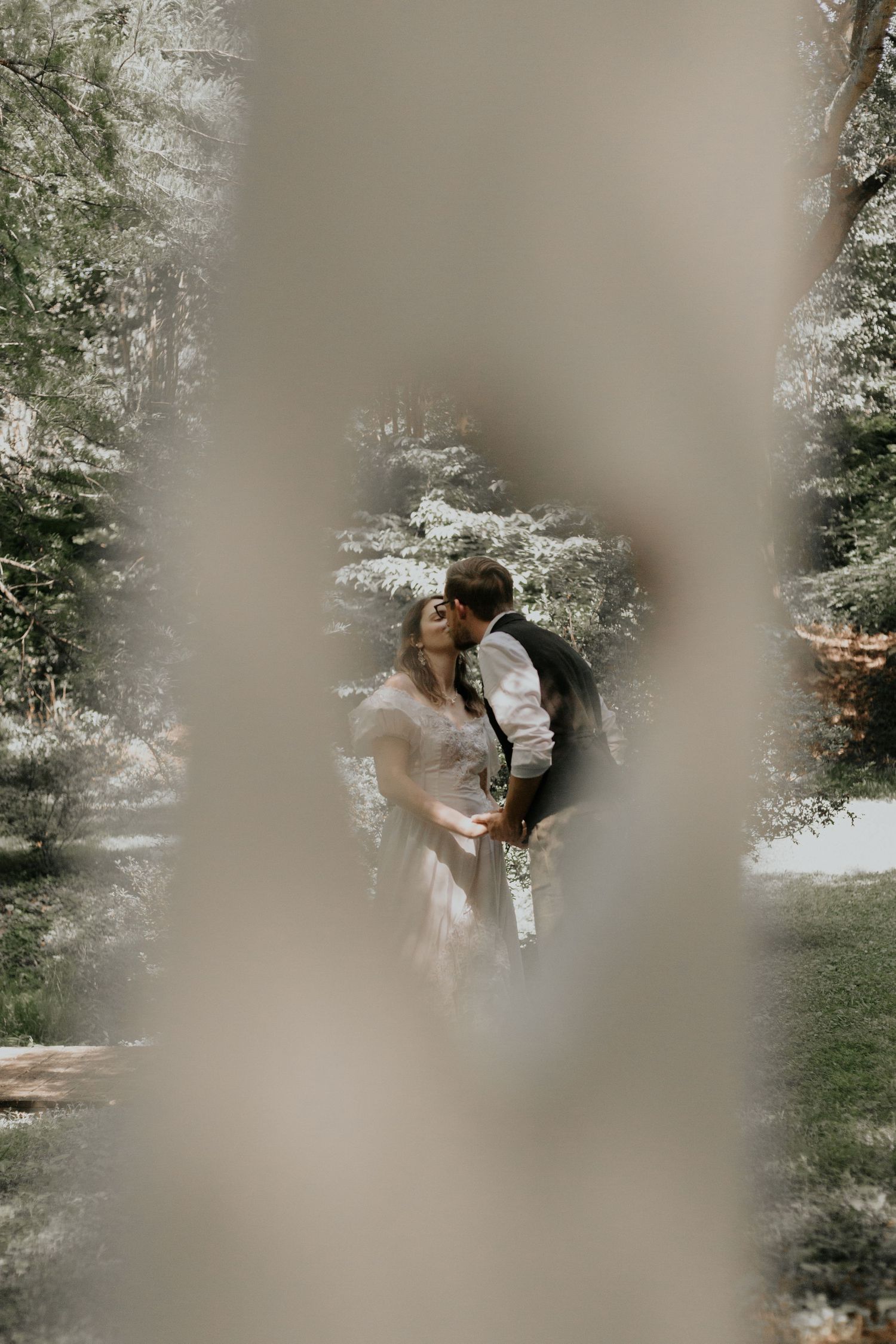 Bride and groom sharing a romantic kiss framed by soft bokeh trees in a lush garden setting. kilgore lewis house greenville sc