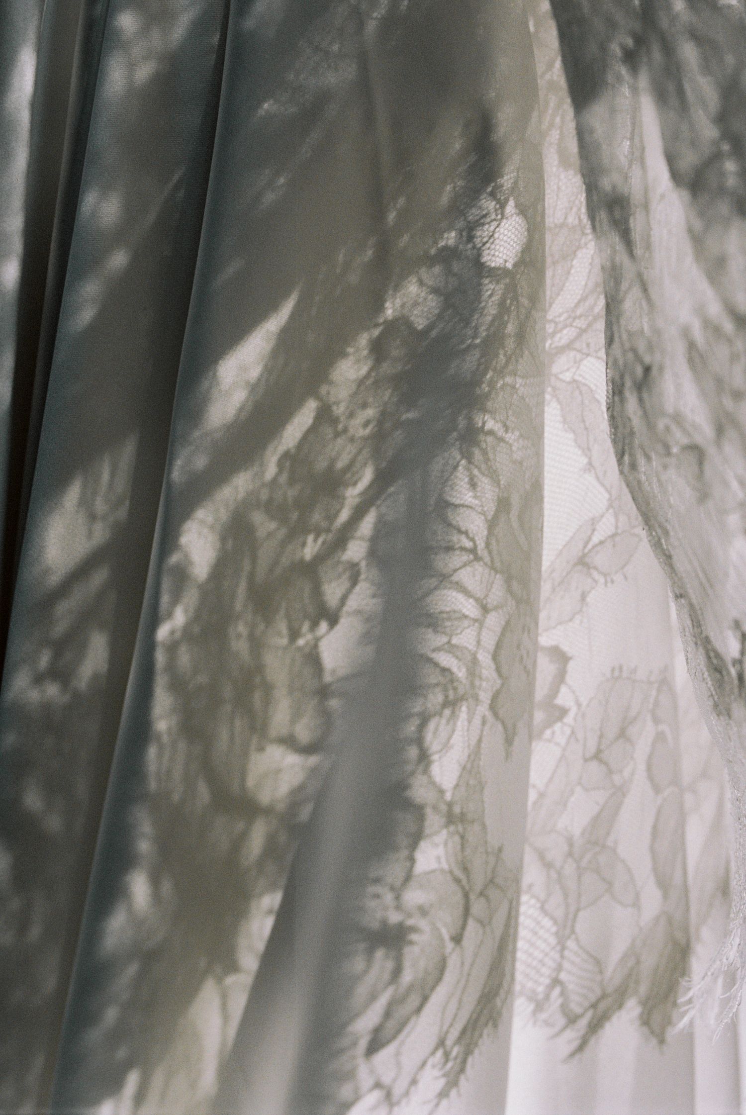 Close-up of elegant white lace wedding dress fabric with delicate floral patterns and soft natural light shadows.
