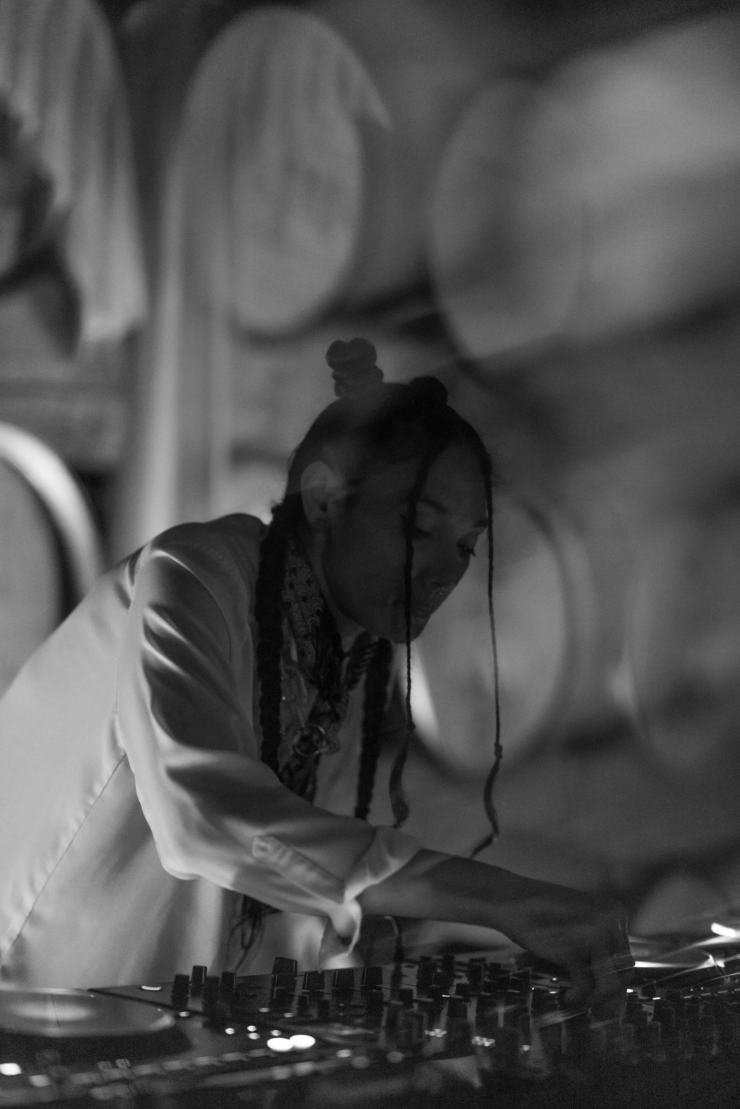 Black and white photo of a female DJ with braids performing at a venue with barrel decor.