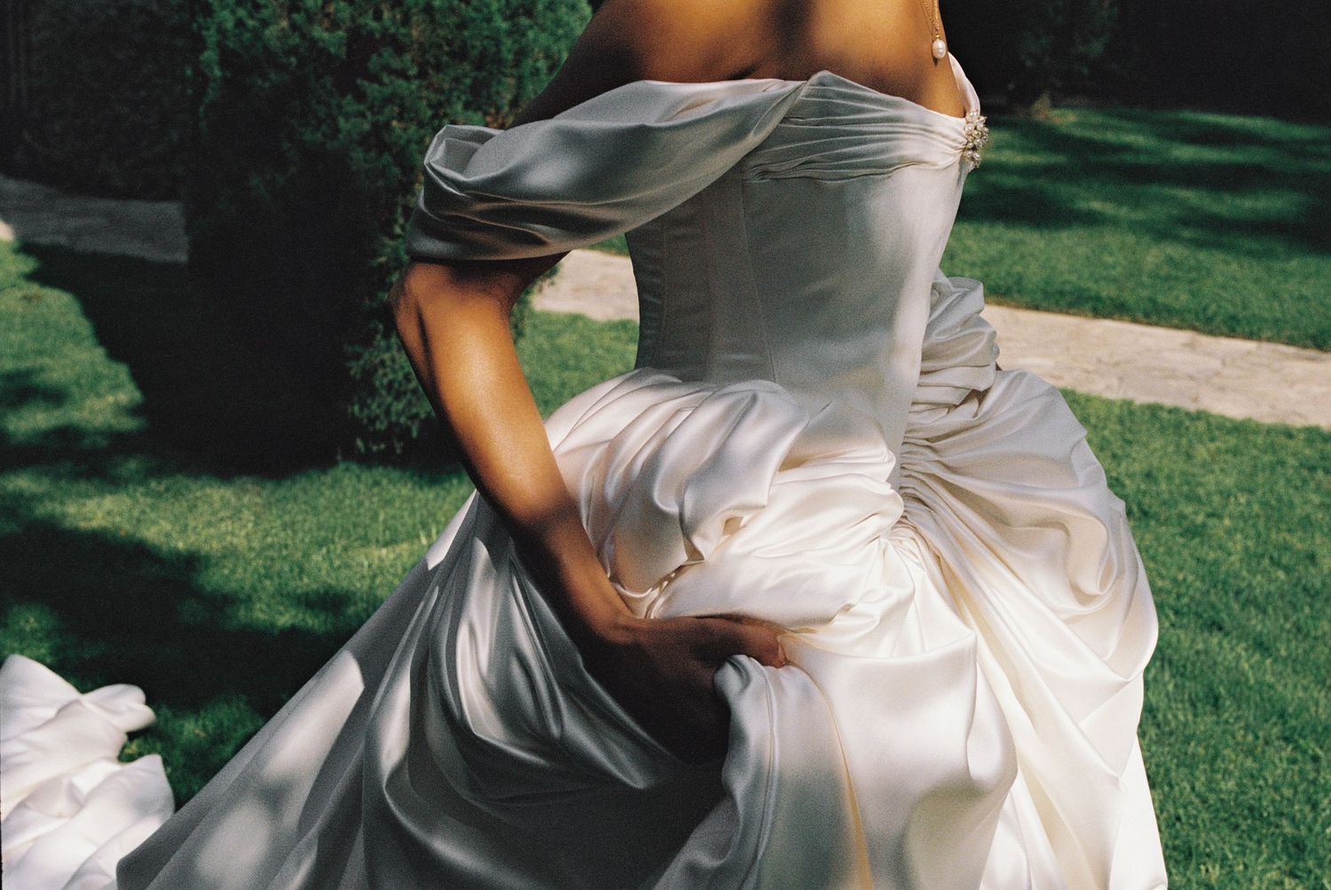 Bride in elegant strapless white satin ball gown wedding dress, standing in lush green garden.